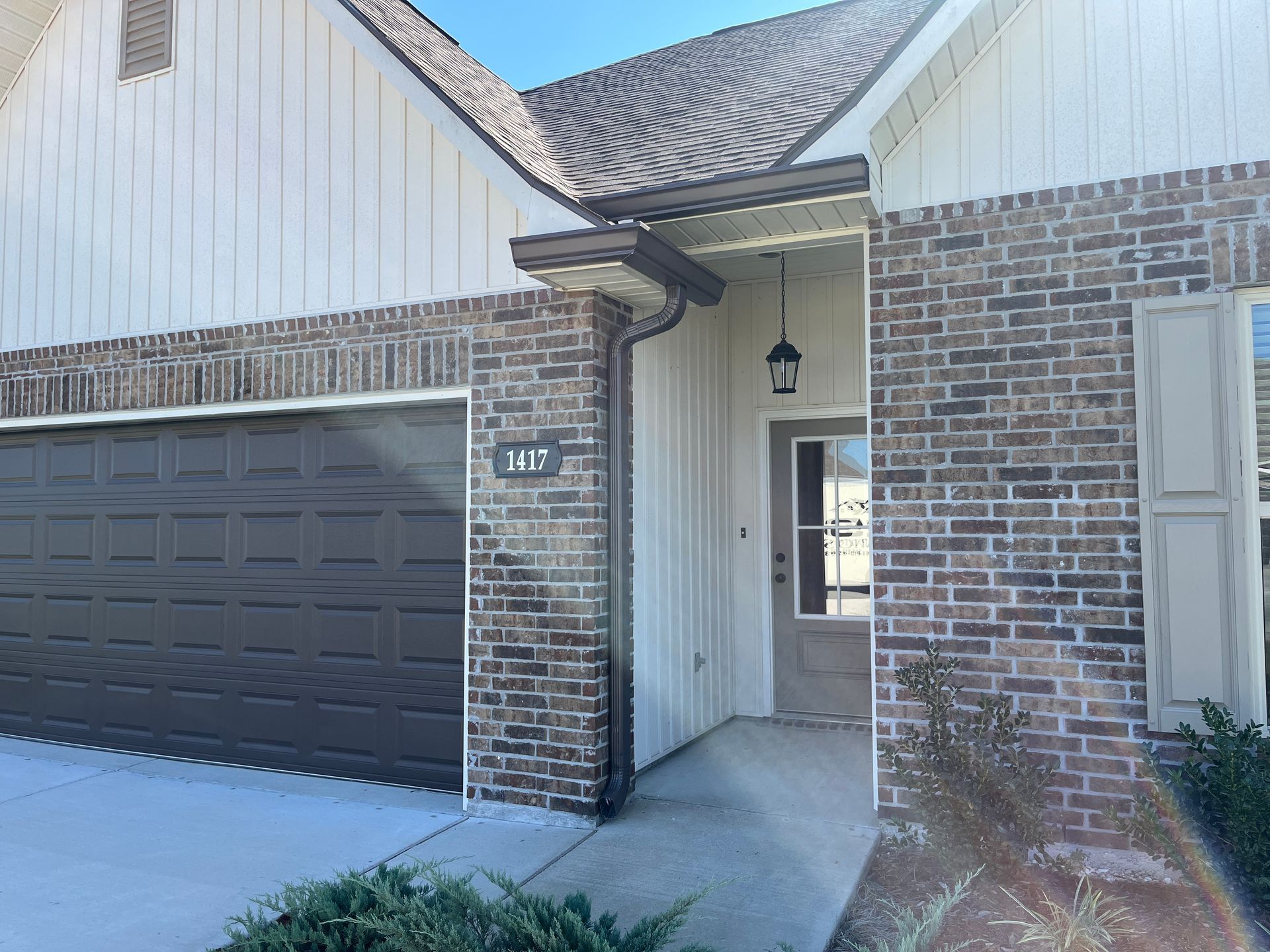 A single-story suburban home exterior with brick and white siding, a dark garage door, and a front entryway.