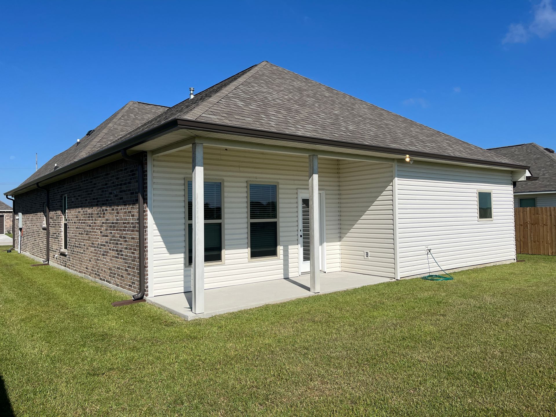 Back view of a one-story suburban house with a covered concrete patio, light siding, and gray brick side walls.