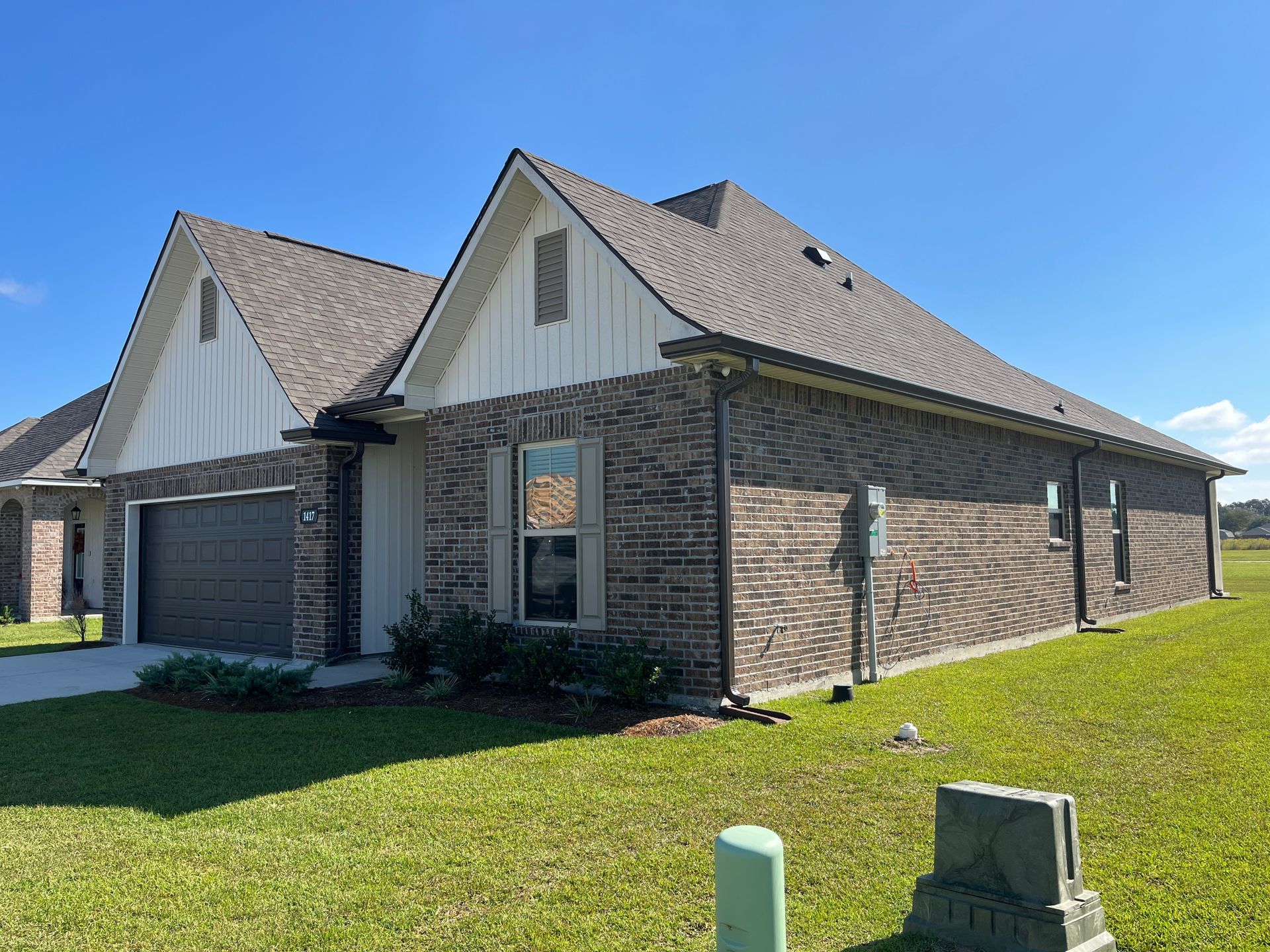 A side view of a suburban brick house with white vertical siding on the gables, a grey roof, and a dark garage door.