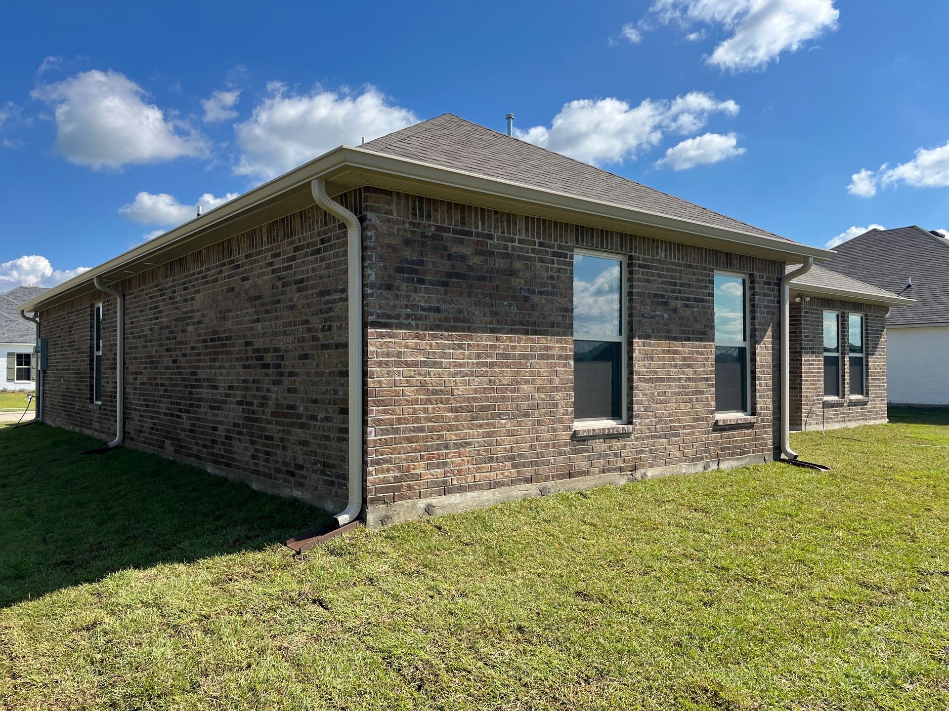 A single-story brick house with a hip roof and two windows on a grassy lawn under a sunny blue sky.