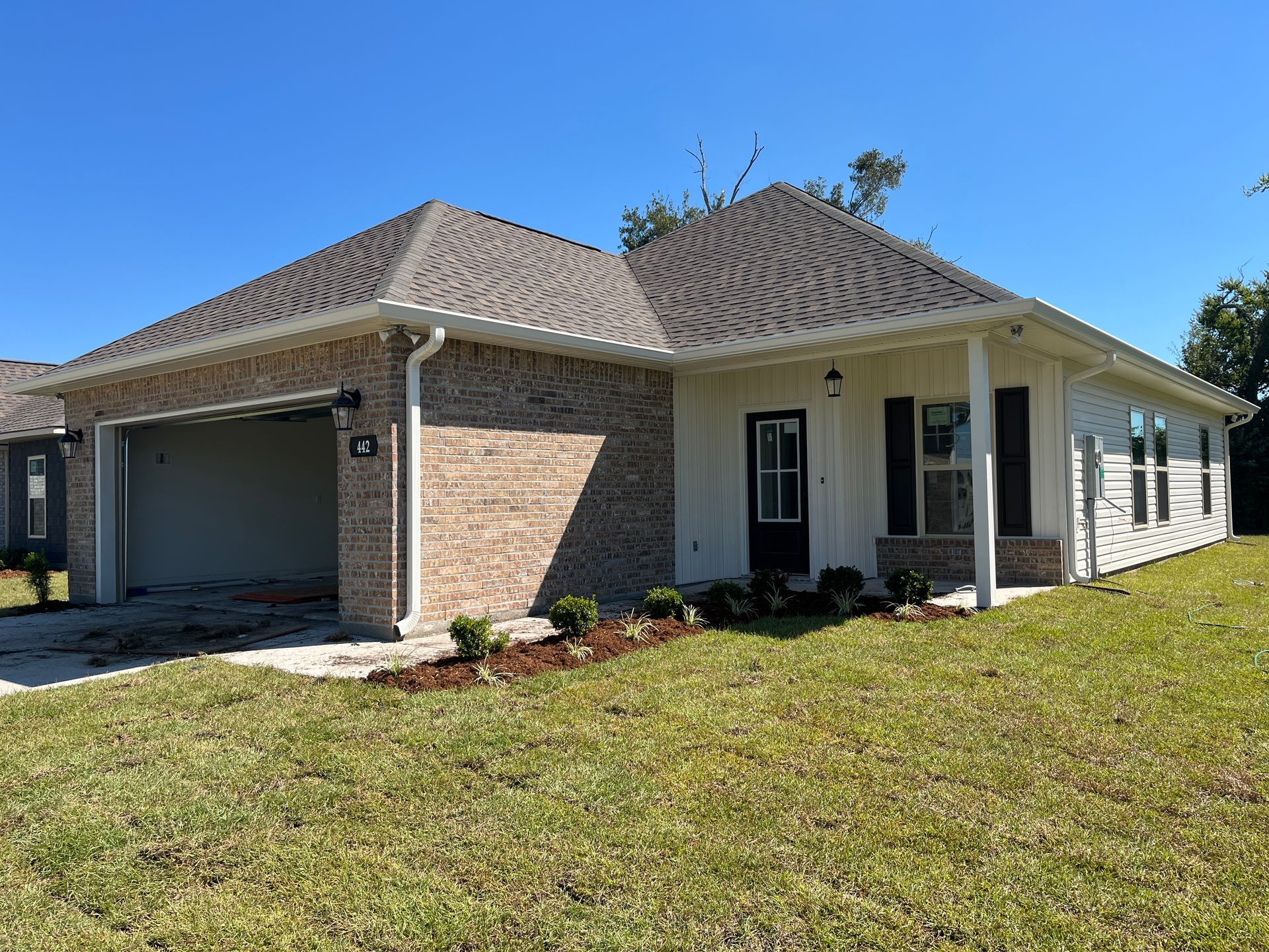 Single-story brick and white siding house with a two-car garage under a hip roof on a sunny day.