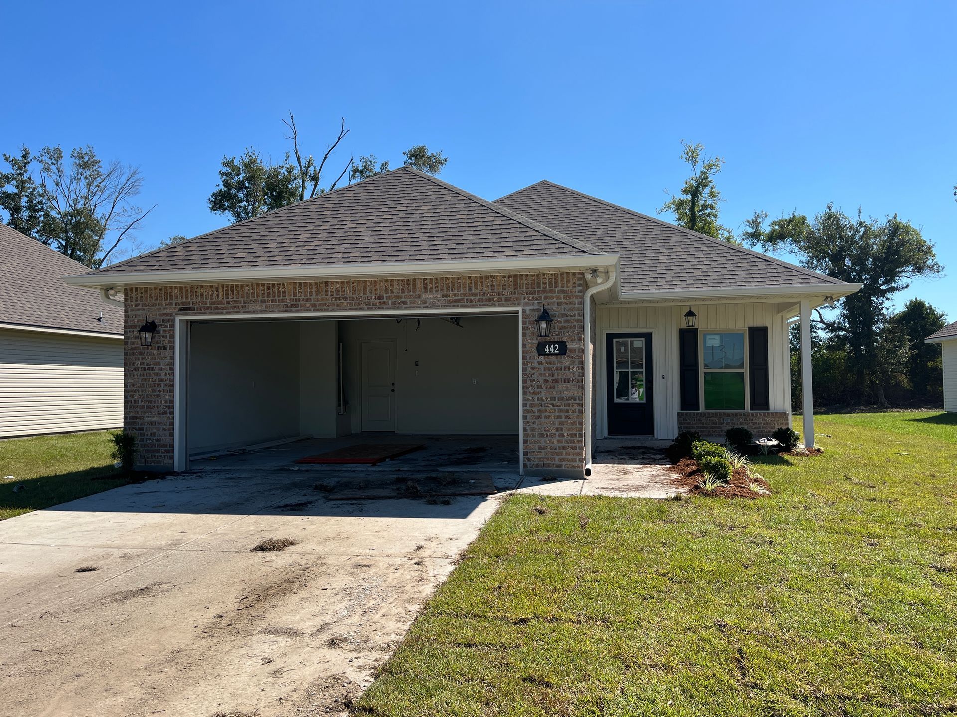 A single-story, tan brick suburban house with a dark roof, attached garage, and front entrance, set on a grassy lawn.