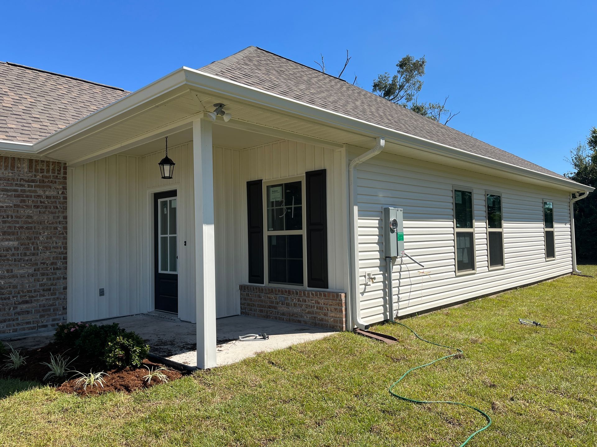 Side view of a house with white horizontal and vertical siding, a covered porch entrance, and a brown shingled roof.