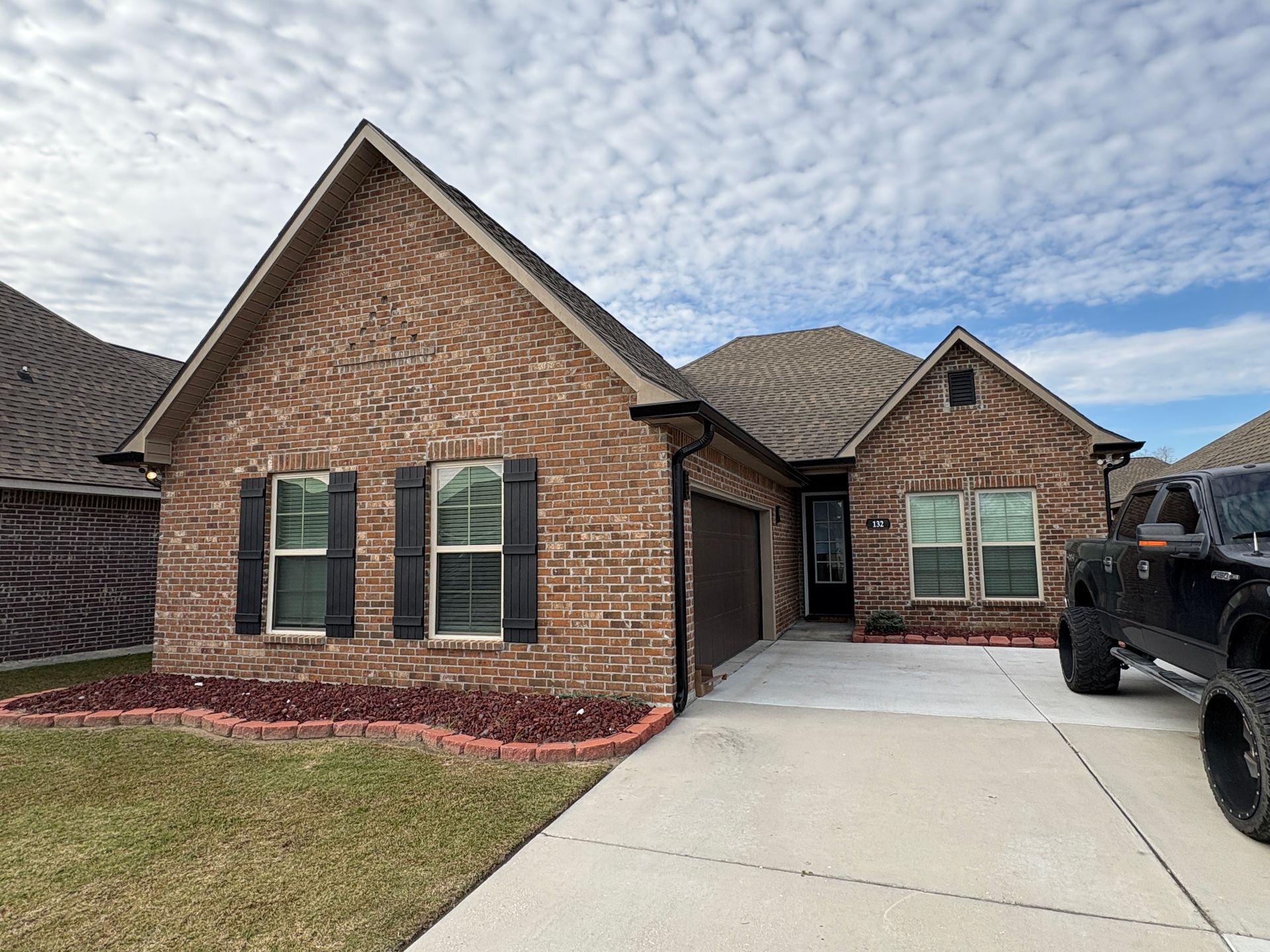 A brown brick, single-story suburban house with a driveway, attached garage, and a black truck parked to the side.