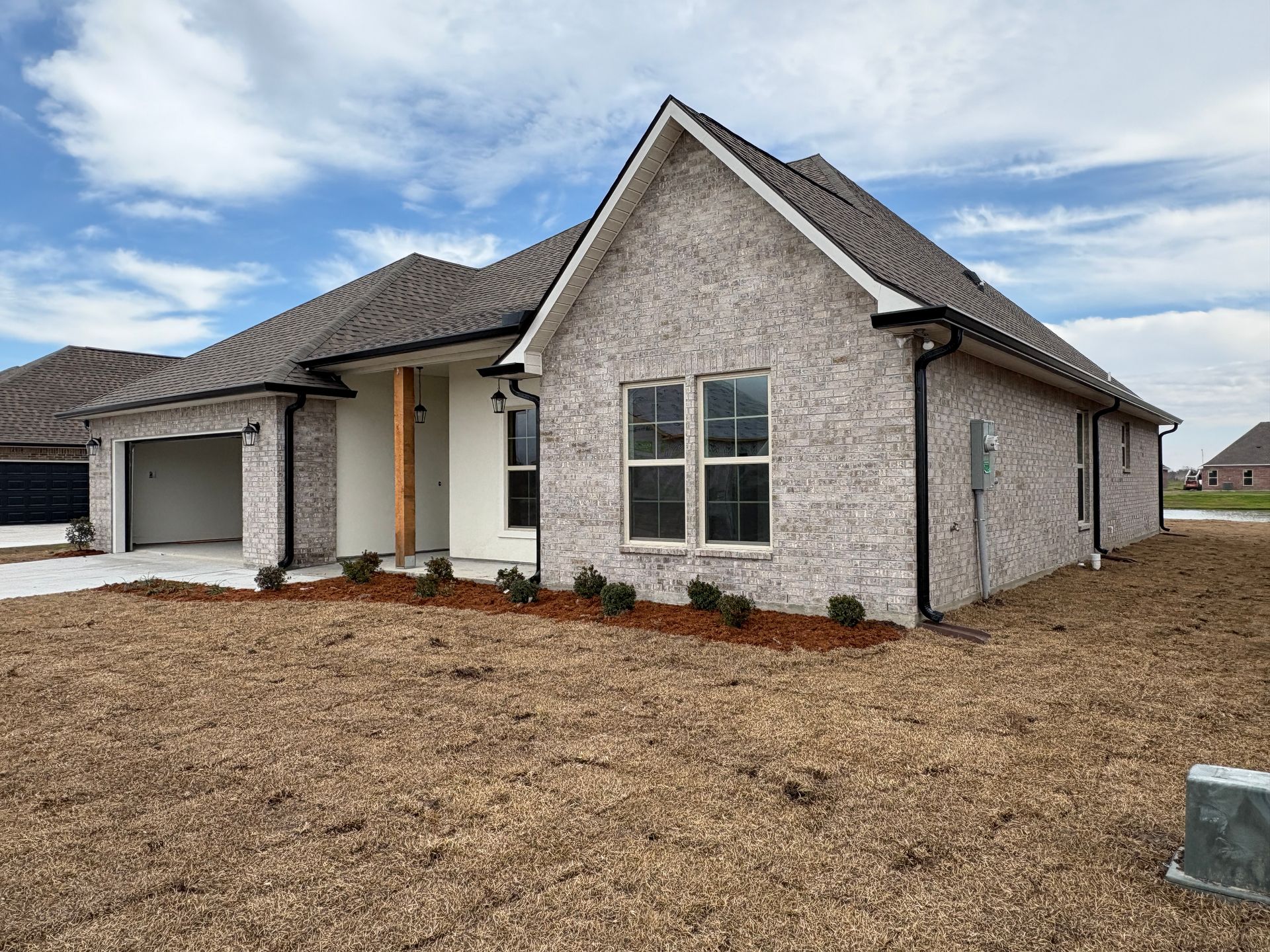 A single-story, light gray brick house with a dark gabled roof, an attached garage, and a newly landscaped front yard.