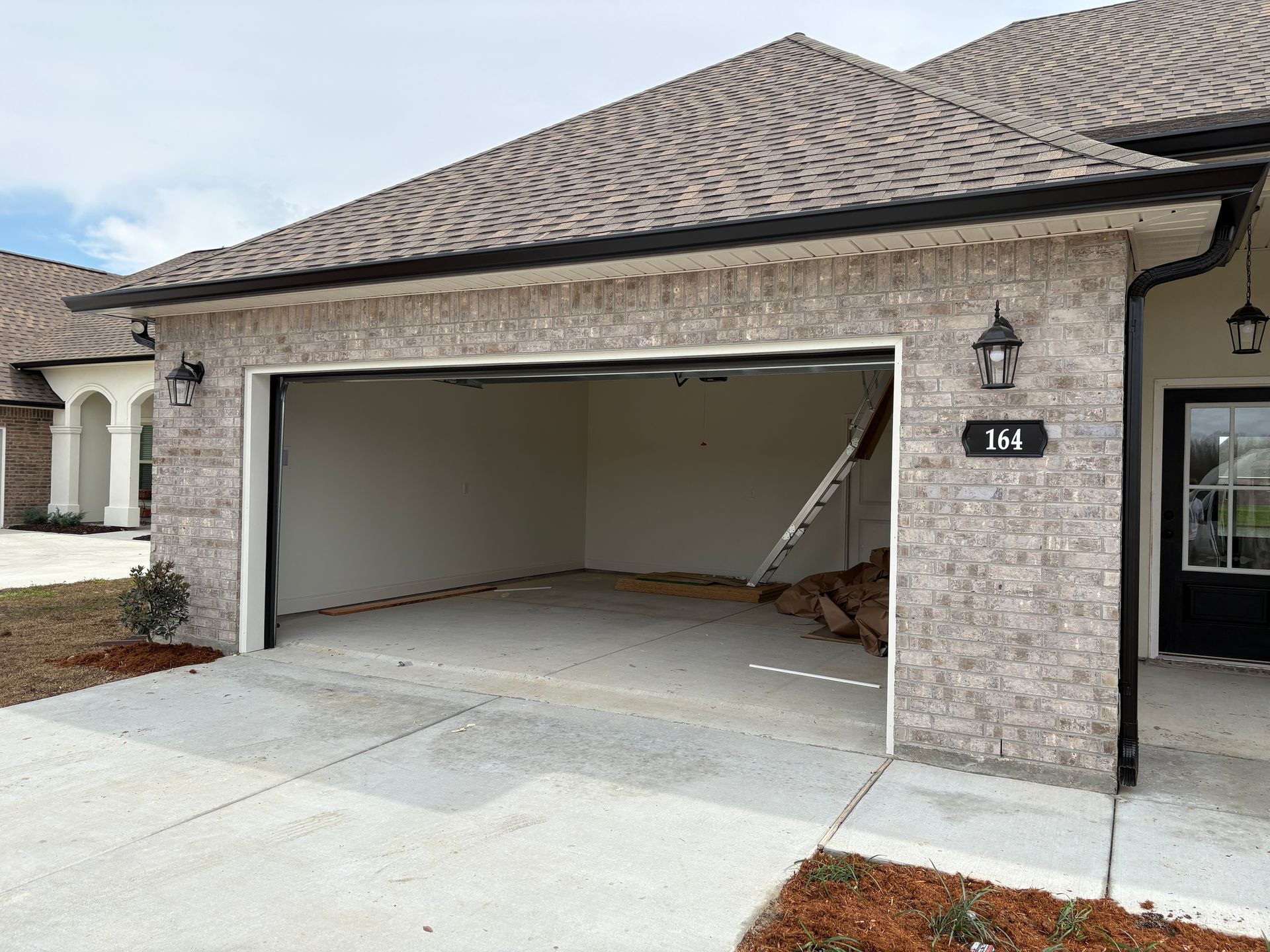 A light-colored brick house exterior featuring an open, empty garage and a black front door with the number 164.