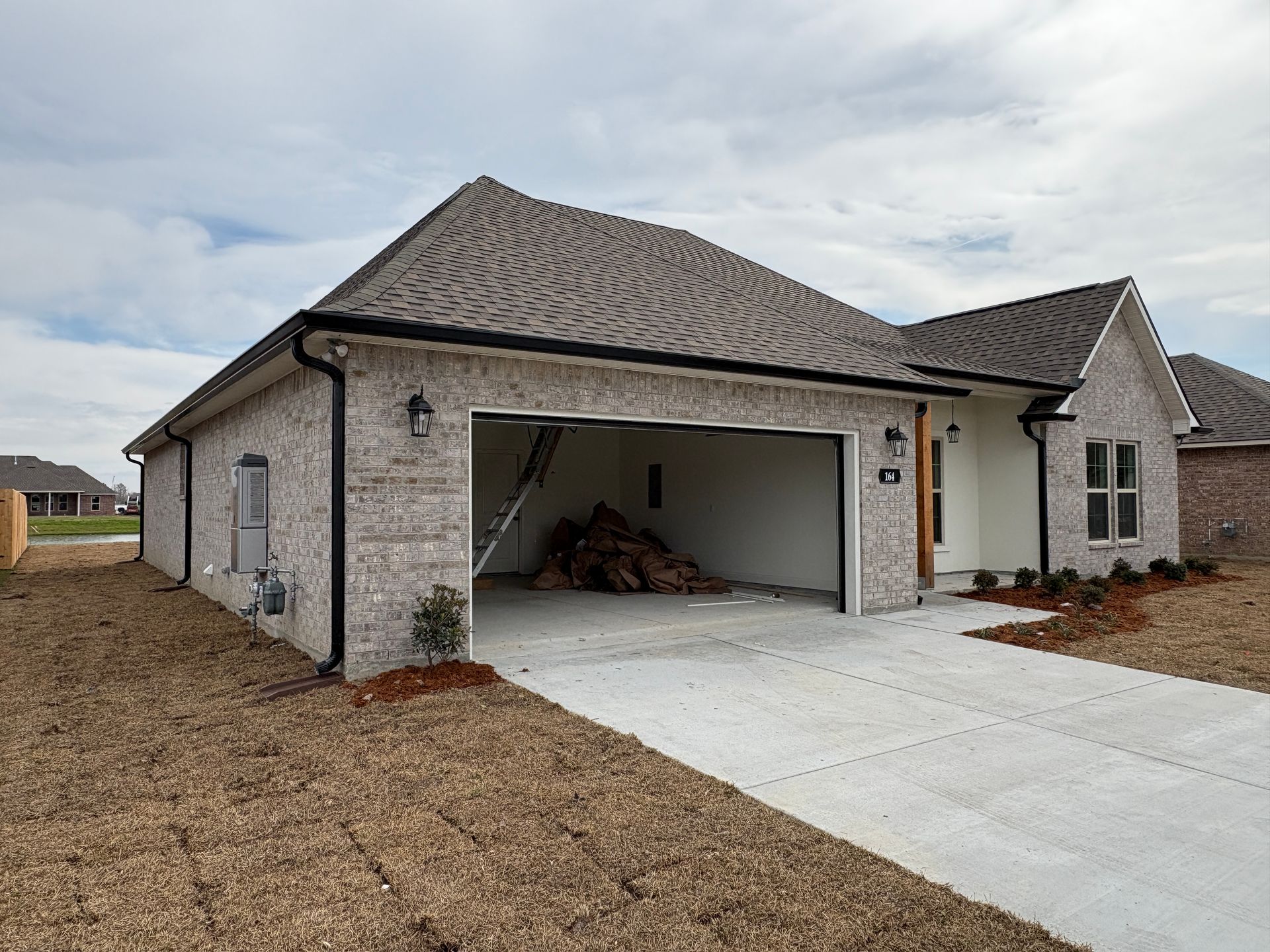 A light-colored brick house under construction with an open garage, a concrete driveway, and unfinished landscaping.