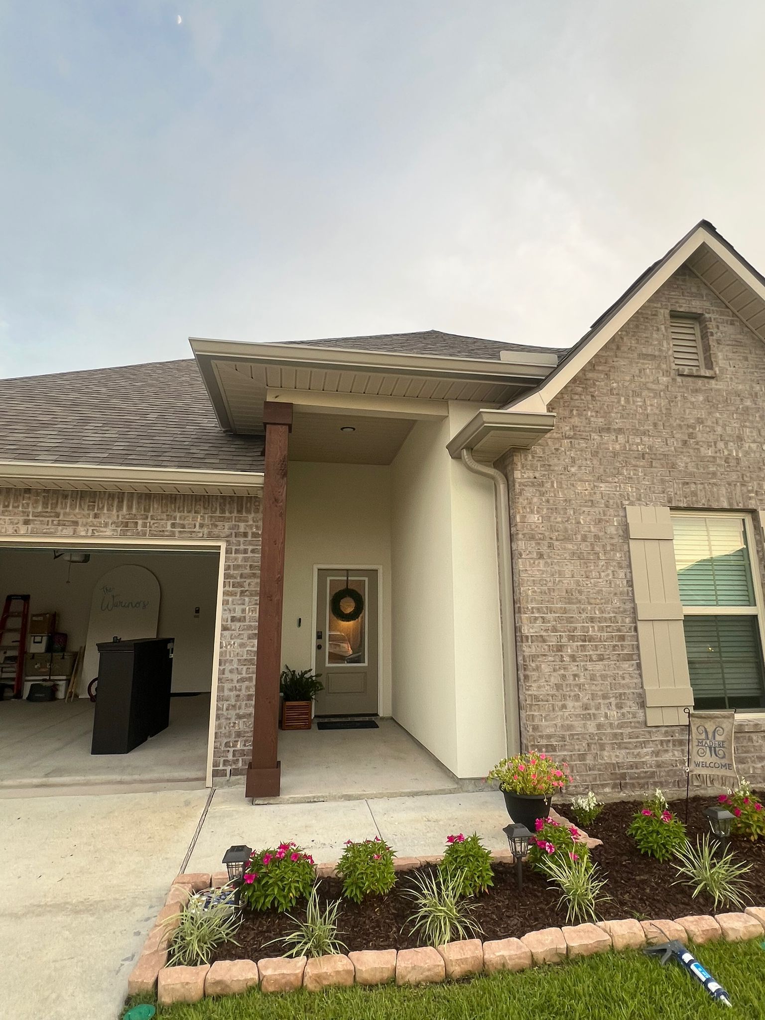 A modern suburban brick home with a recessed entryway, a dark wooden support post, and a landscaped front flower bed.