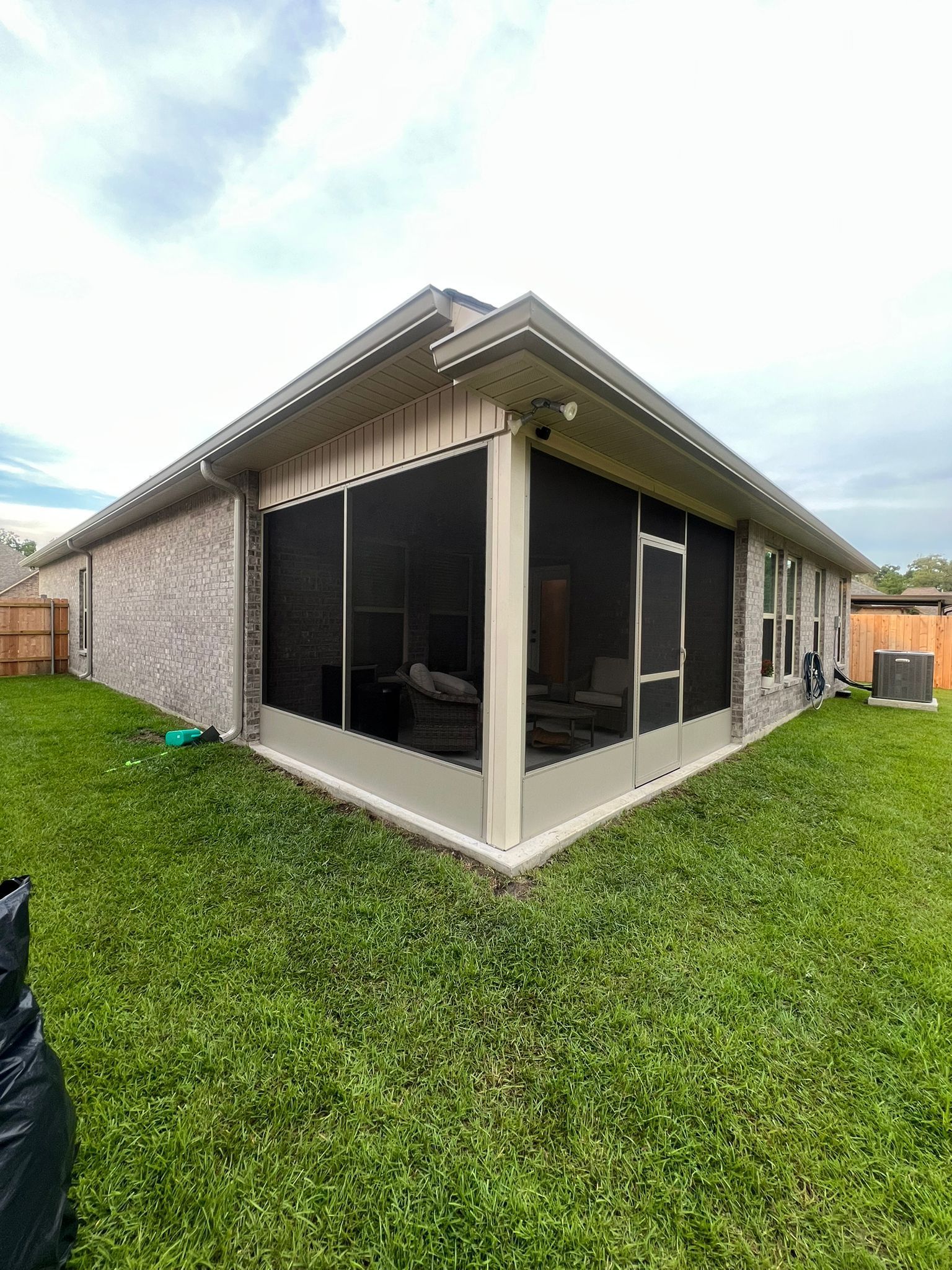 A corner view of a light-colored brick house featuring a screened-in back porch with cream trim and a door.