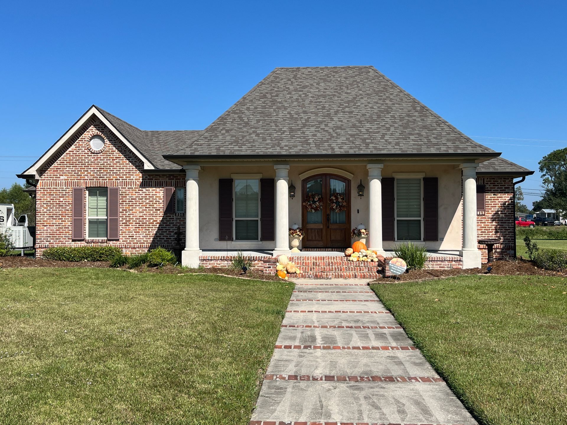 A single-story brick house with a front porch, columns, and a sidewalk leading to the front door under a clear blue sky.