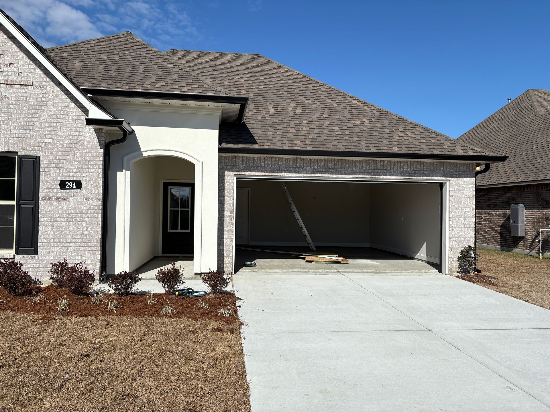 A newly built single-story brick home with a white arched entryway, dark shutters, and an open garage.