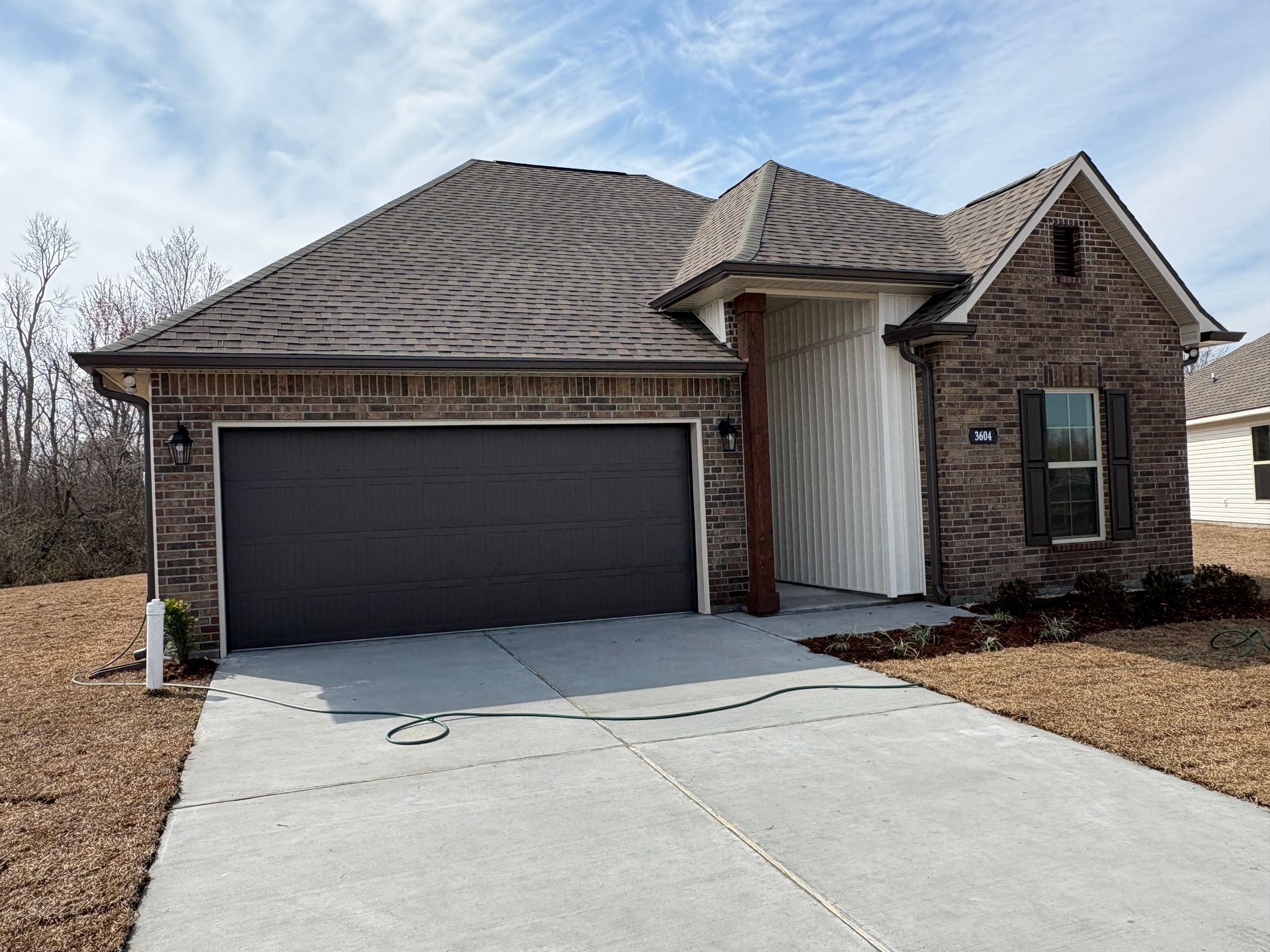 A single-story brick house with a dark garage door, a front porch area with vertical siding, and a concrete driveway.