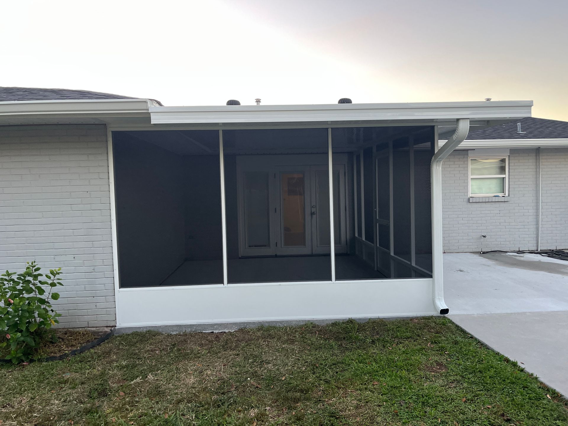 A gray, single-story house featuring a newly installed white-framed screened-in patio enclosure.