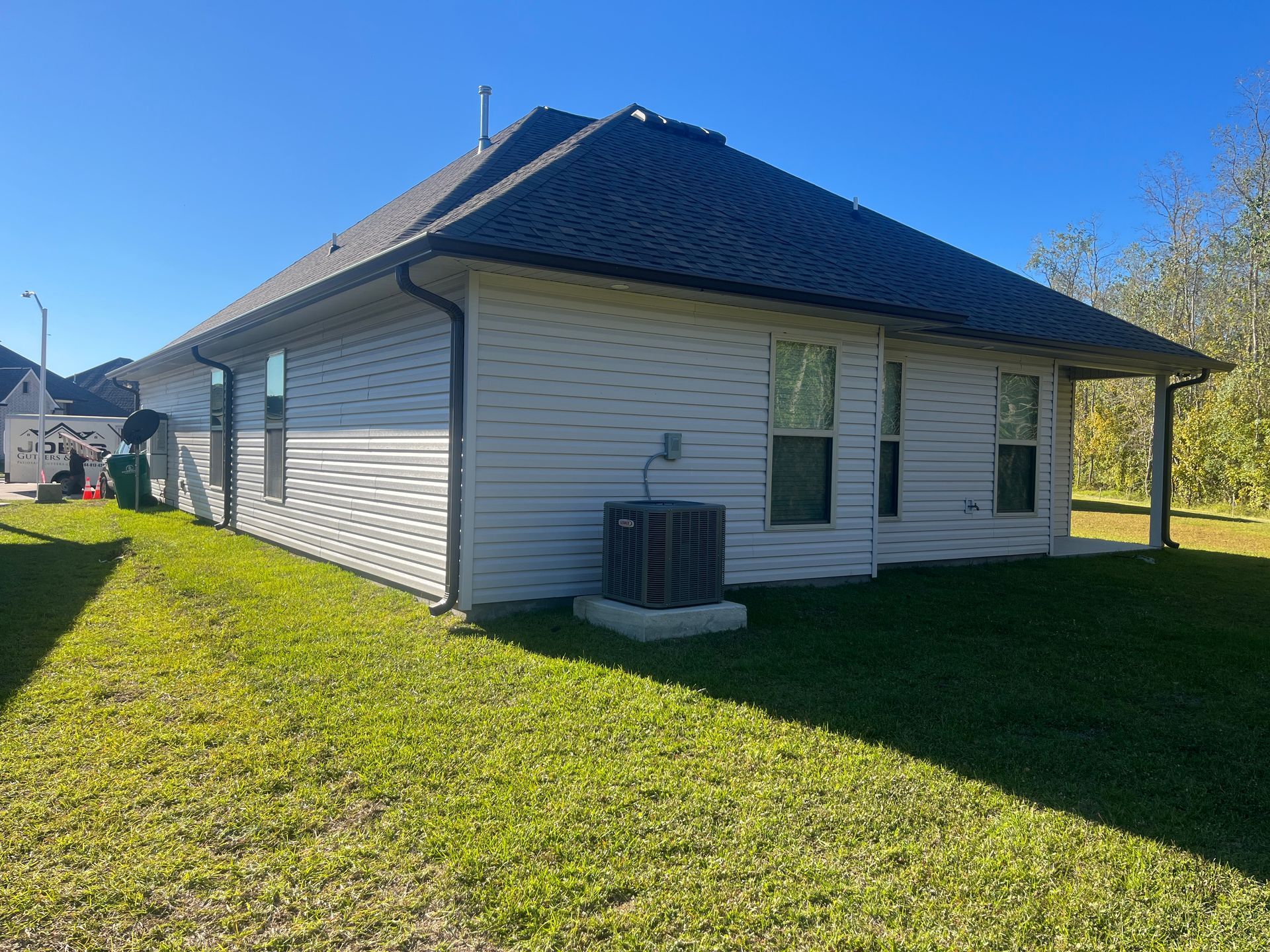 A view of the side and back of a light-colored, single-story vinyl siding house with a dark roof and an AC unit outside.