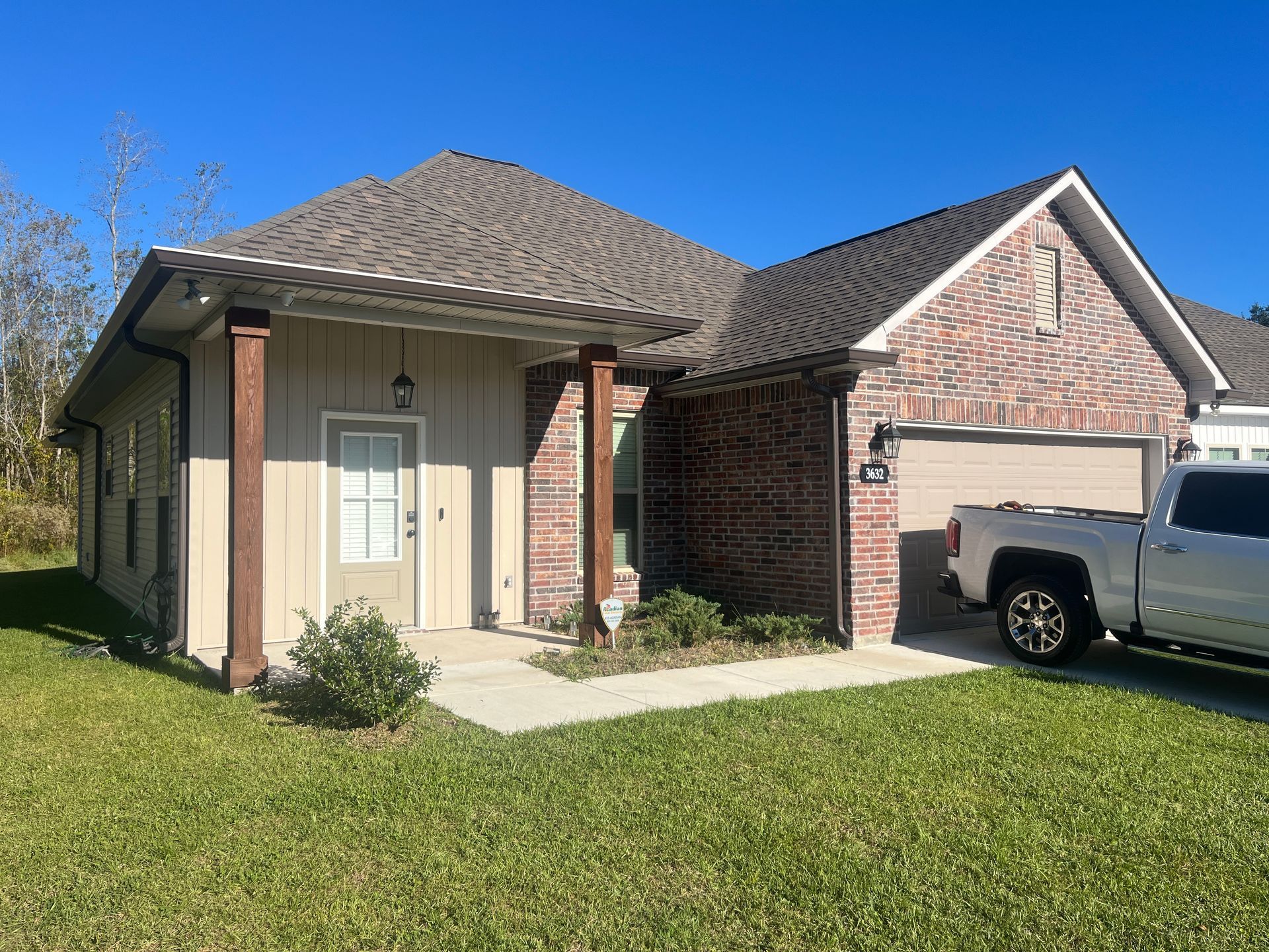 A beige and brick single-story house with a front porch, wood columns, and an attached garage parked with a white truck.