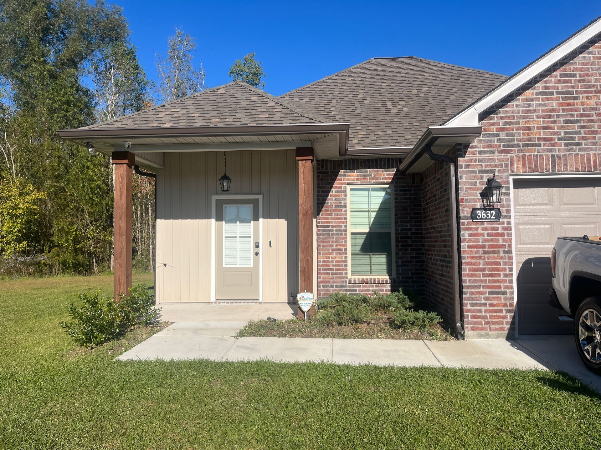 A front view of a single-story brick home with a covered entryway, a wooden front door, and a partial view of a garage.