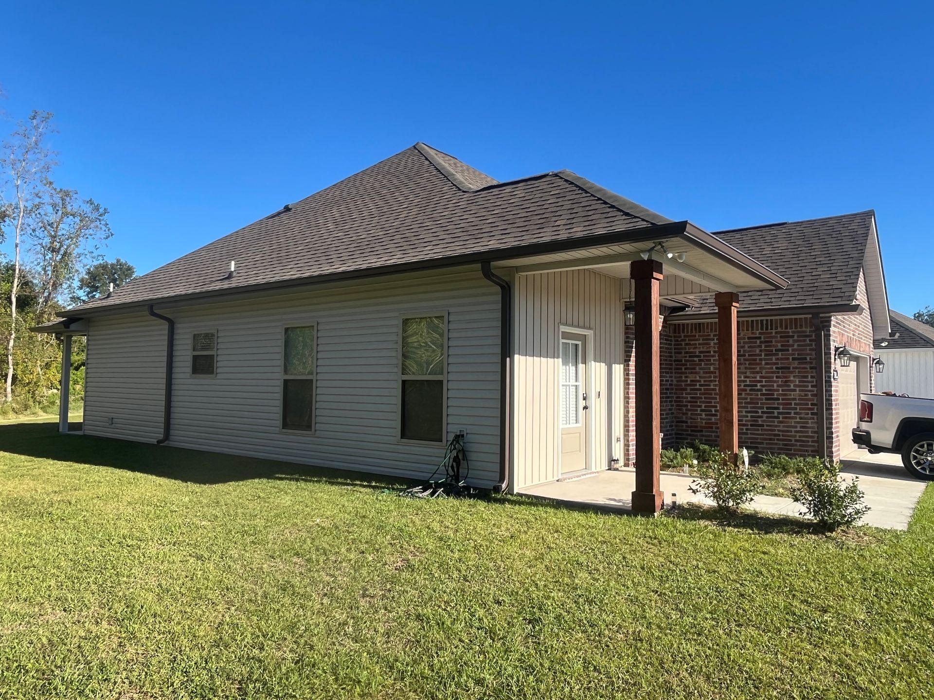 A light-colored house with a dark roof and a brick-accented porch, set in a sunny lawn under a clear blue sky.