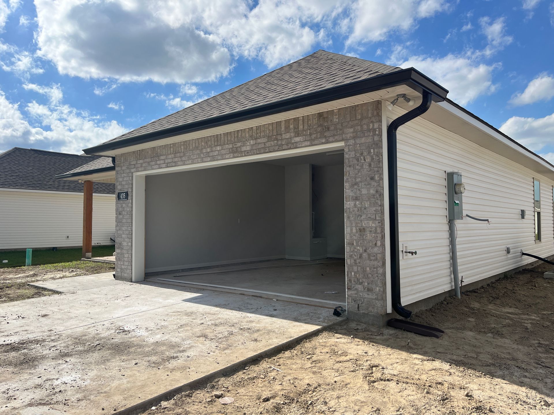 An open two-car garage of a new construction home featuring grey brick siding and white horizontal trim under a blue sky.