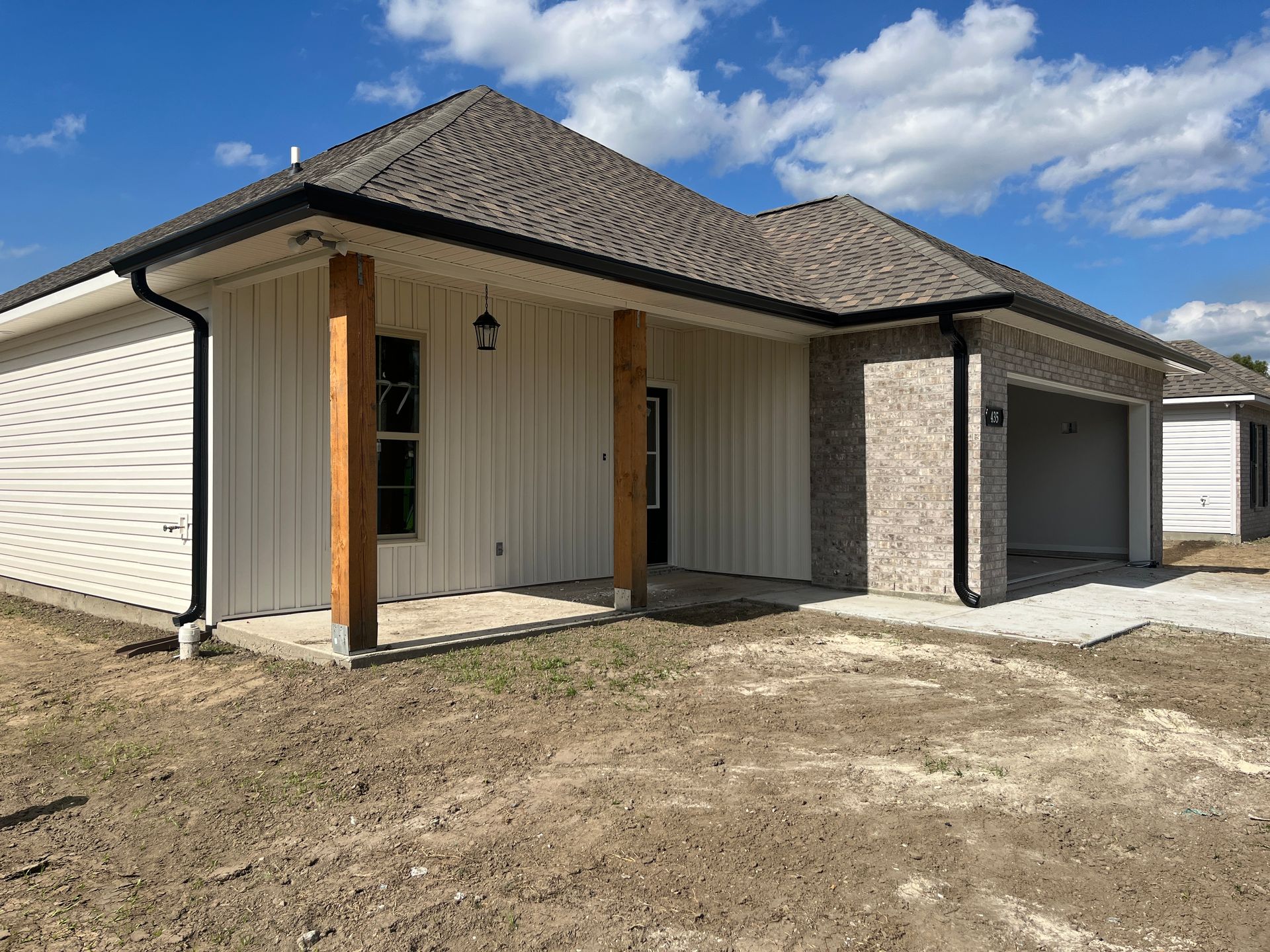 A single-story house exterior with light-colored siding, a stone-front garage, and a covered porch with two wood pillars.