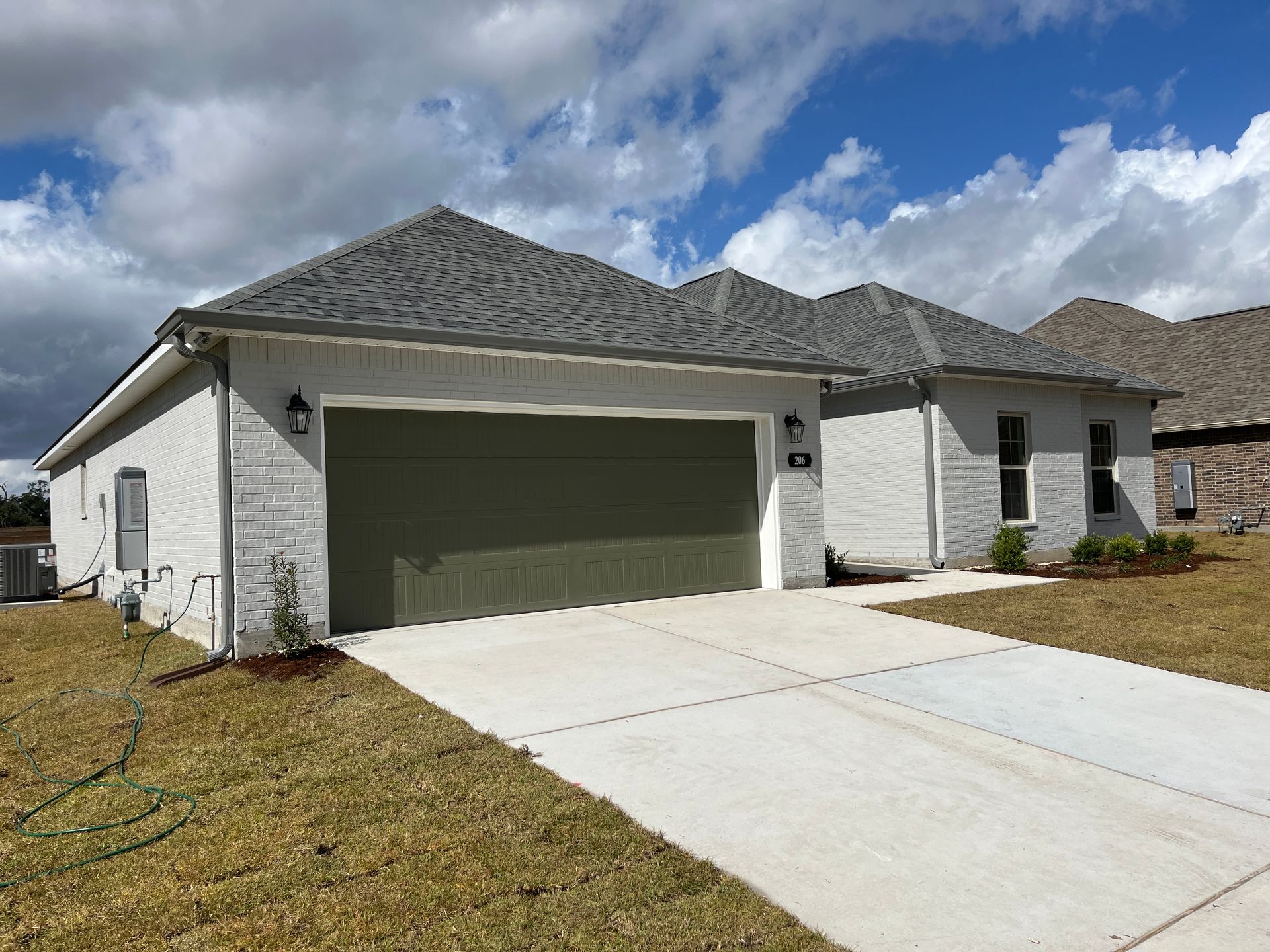 A single-story, light-colored brick suburban house with a dark gray shingled roof, two-car garage, and concrete driveway.