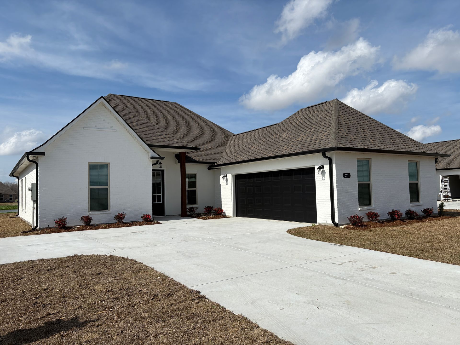 A single-story white brick house with a dark roof and a two-car black garage door under a blue sky with scattered clouds.
