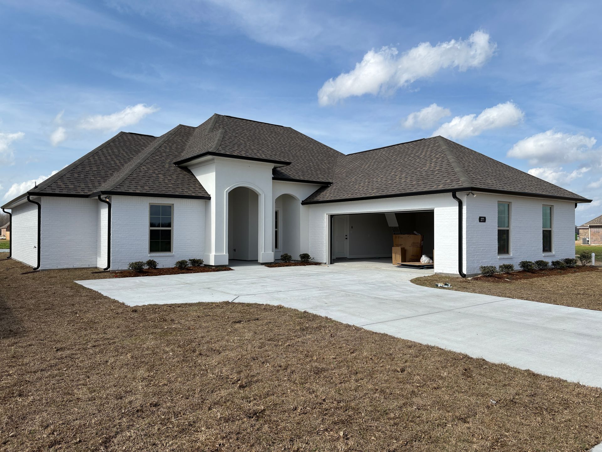 A newly constructed white, one-story house with a dark shingle roof, arched entryway, and an open two-car garage.