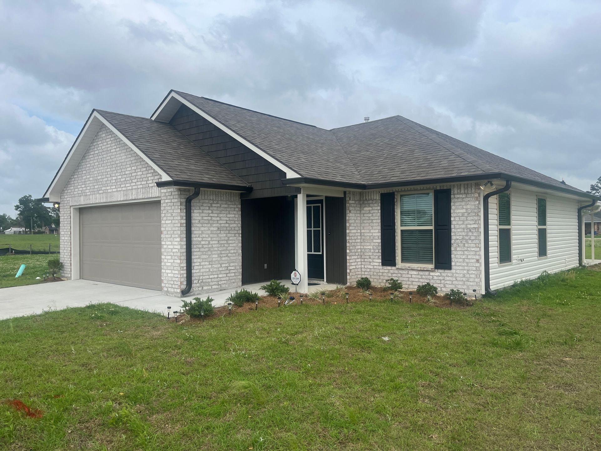 A single-story, white brick house with a brown roof and garage, featuring black accents and a small front yard.