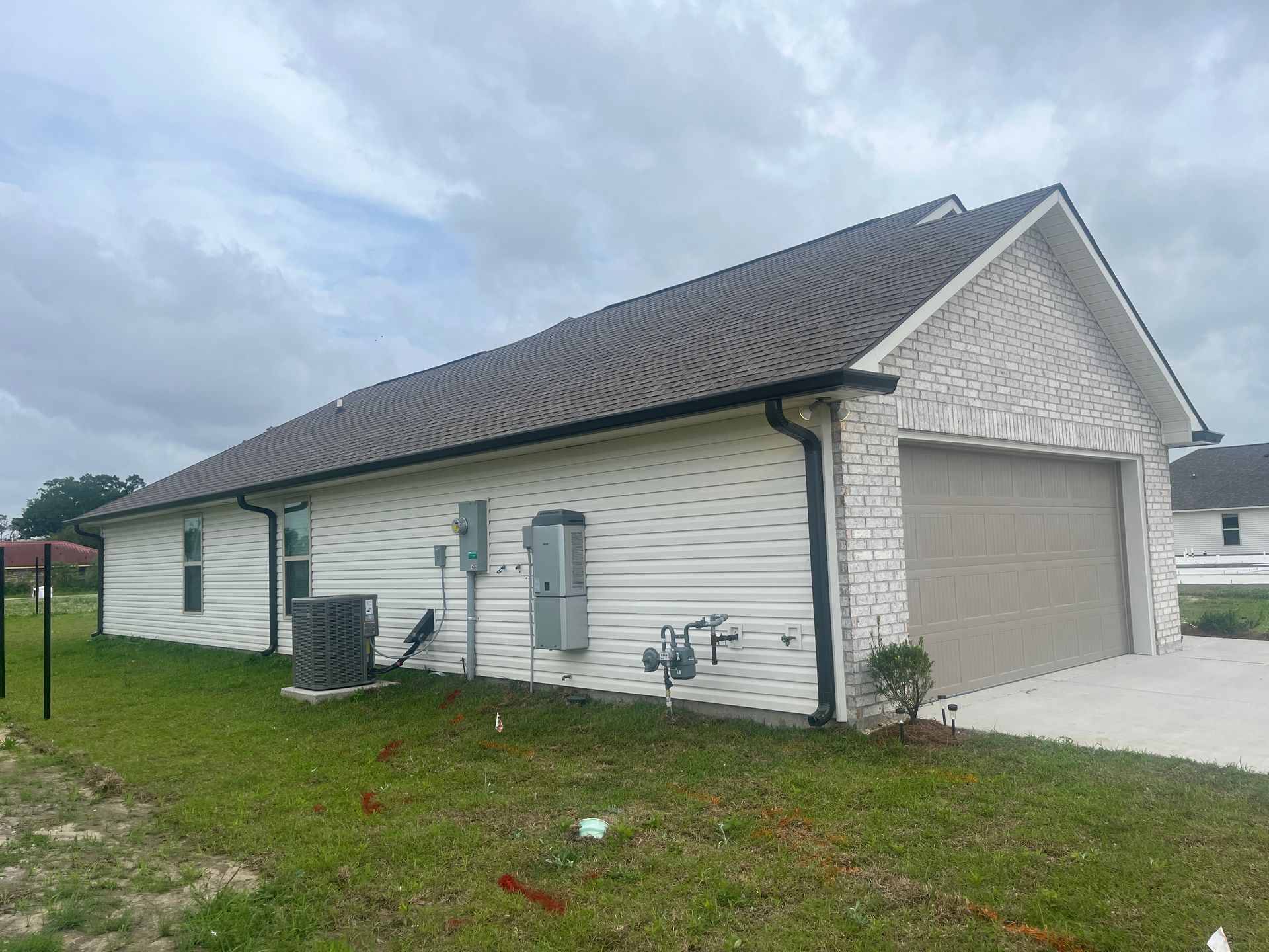 A one-story suburban home with light siding and brick accents, featuring a two-car garage and outdoor utility equipment.