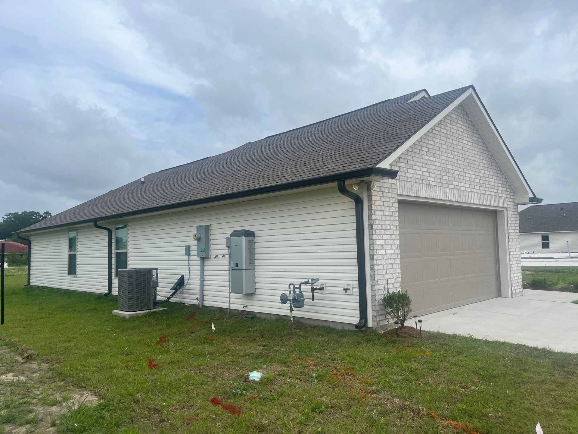 A side view of a house with white horizontal siding and a white brick garage front under a dark shingle roof.