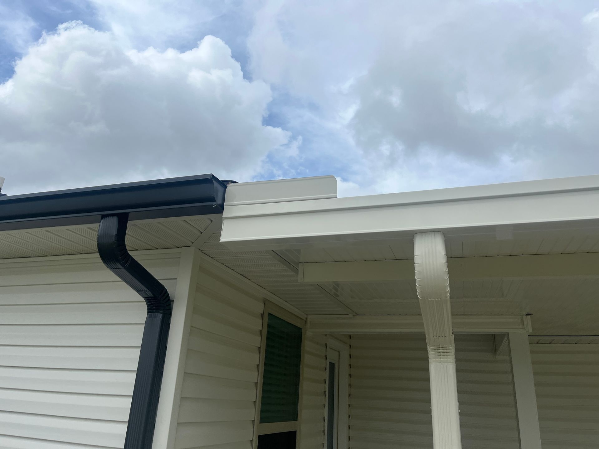 The exterior of a house showing a transition between a dark gutter on the left and a white roofline on the right.