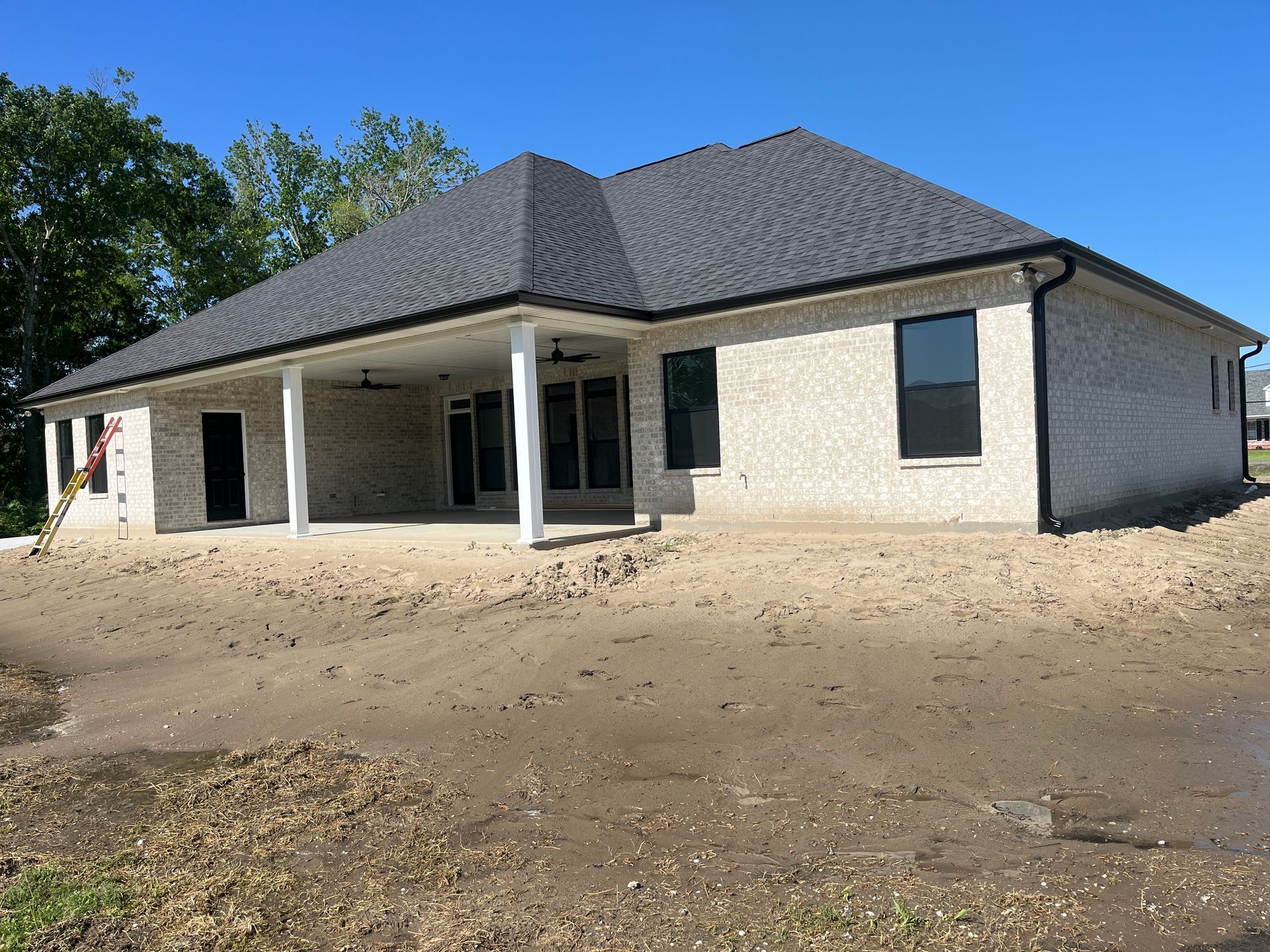 A newly constructed one-story brick house with a dark shingled roof, a covered patio, and unfinished landscaping.