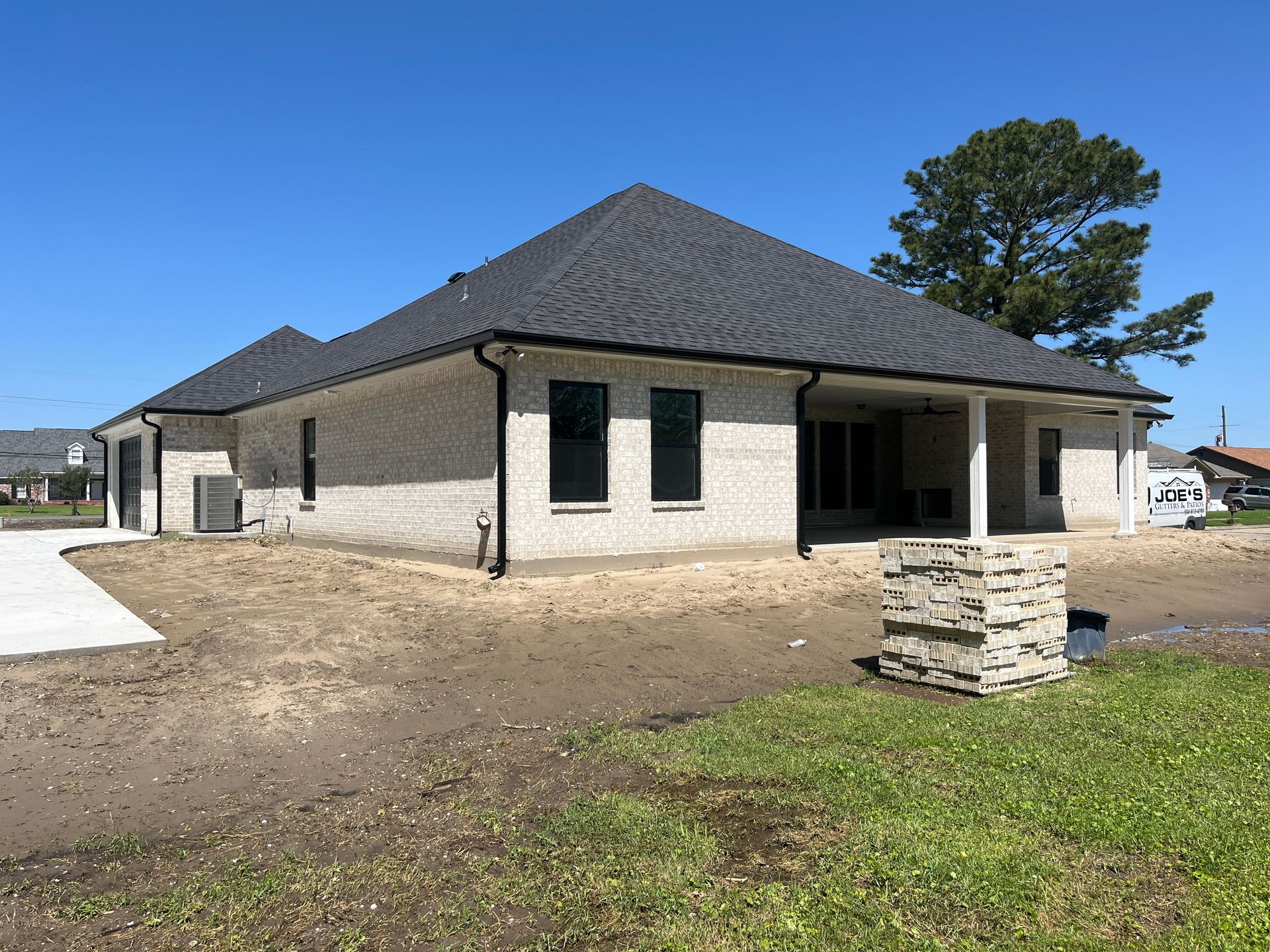 A white brick, single-story house with a dark gray roof sits on an unlandscaped yard under a clear blue sky.