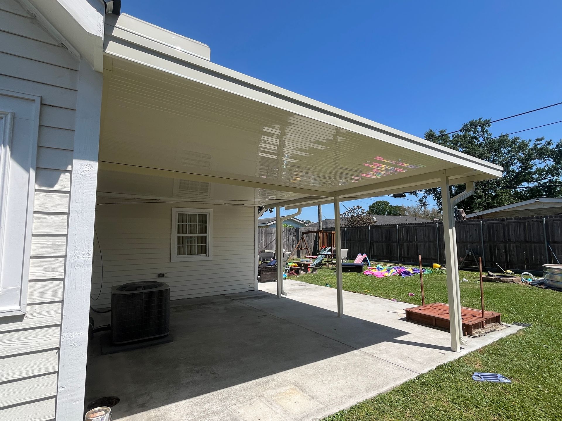 A white home with a beige covered patio, concrete flooring, an air conditioning unit, and a grassy backyard.