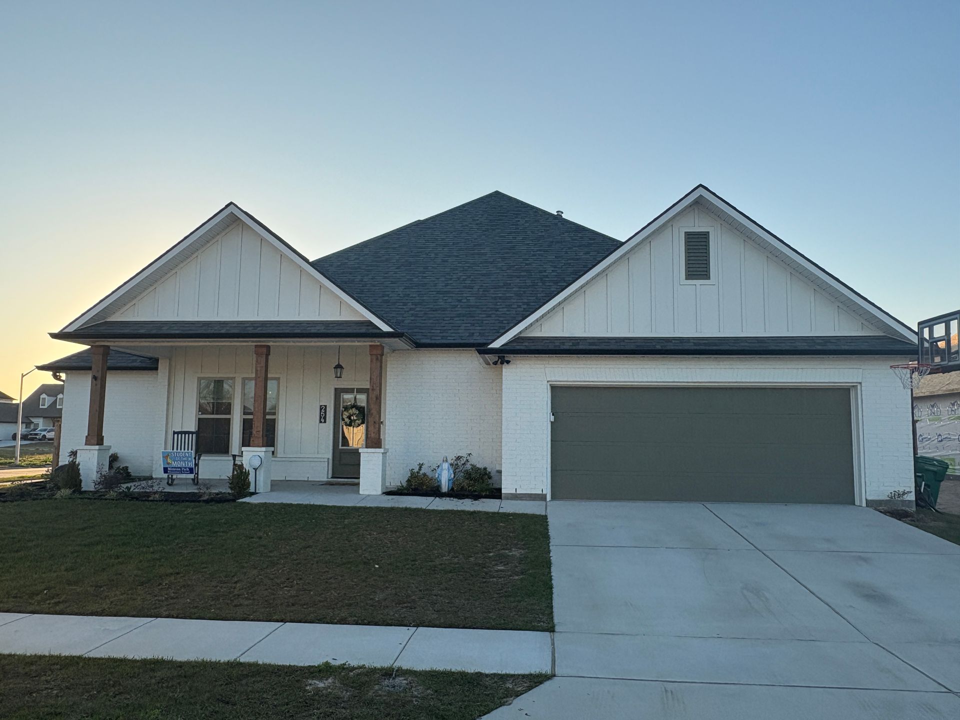 A single-story white house with board-and-batten siding, a gray shingled roof, a front porch, and an attached two-car garage.