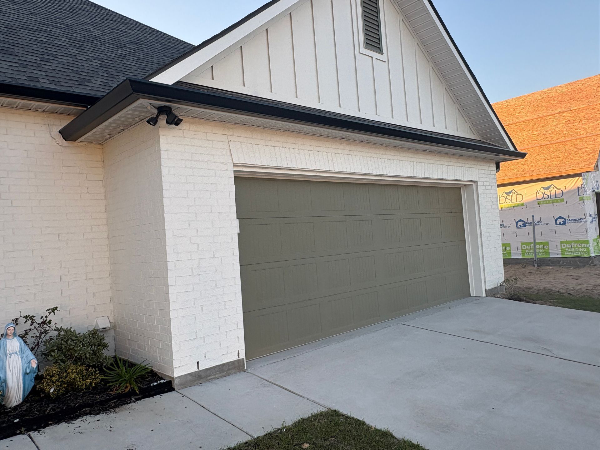 A house exterior featuring a white brick and vertical siding gable with an olive green two-car garage door.