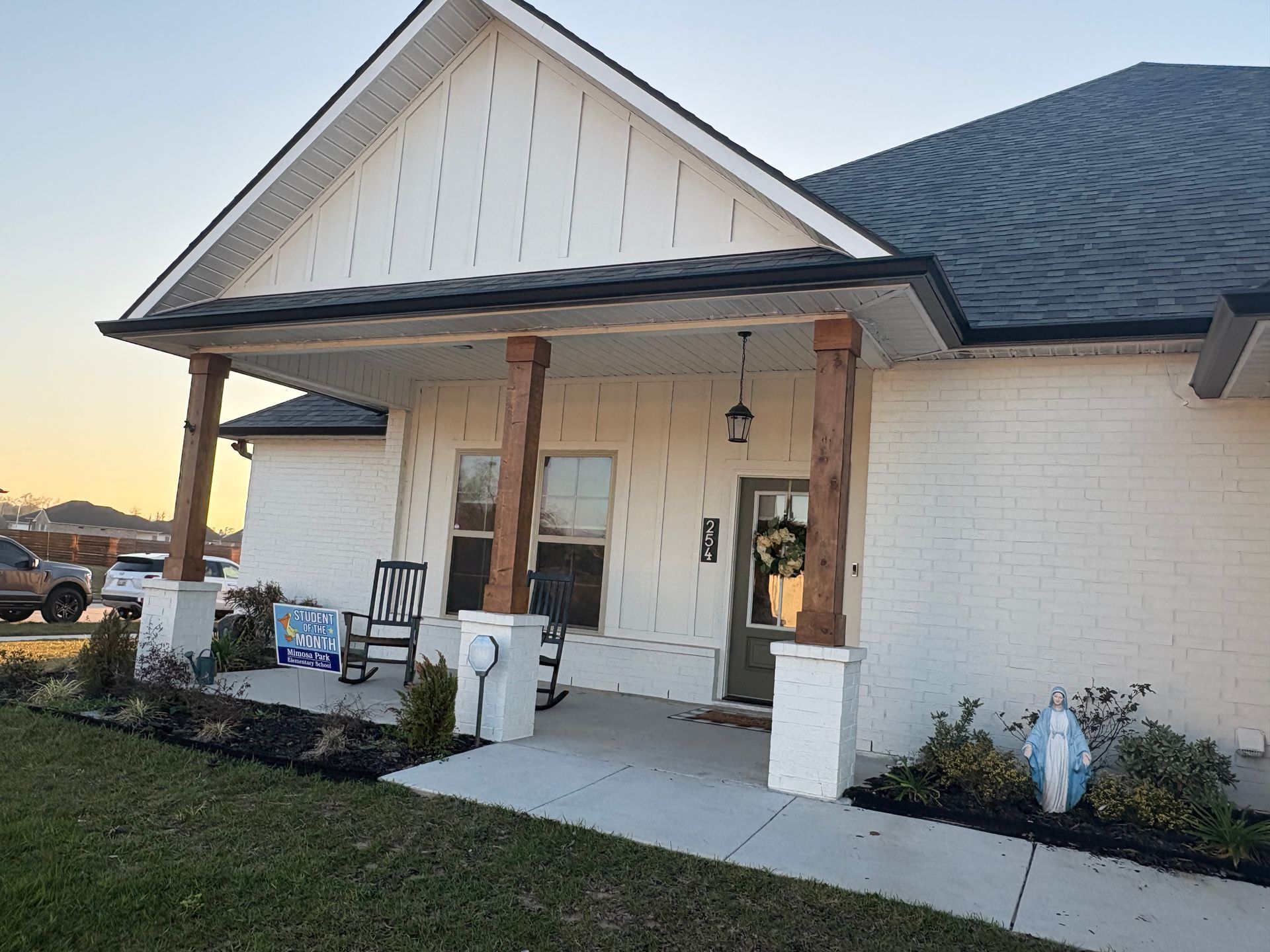 A single-story white brick house with a front porch, featuring two wooden pillars and a white gabled roof.