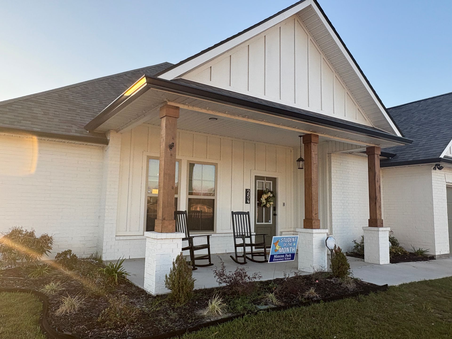 A white home with board-and-batten siding and stone accents features a front porch with wooden columns and rocking chairs.