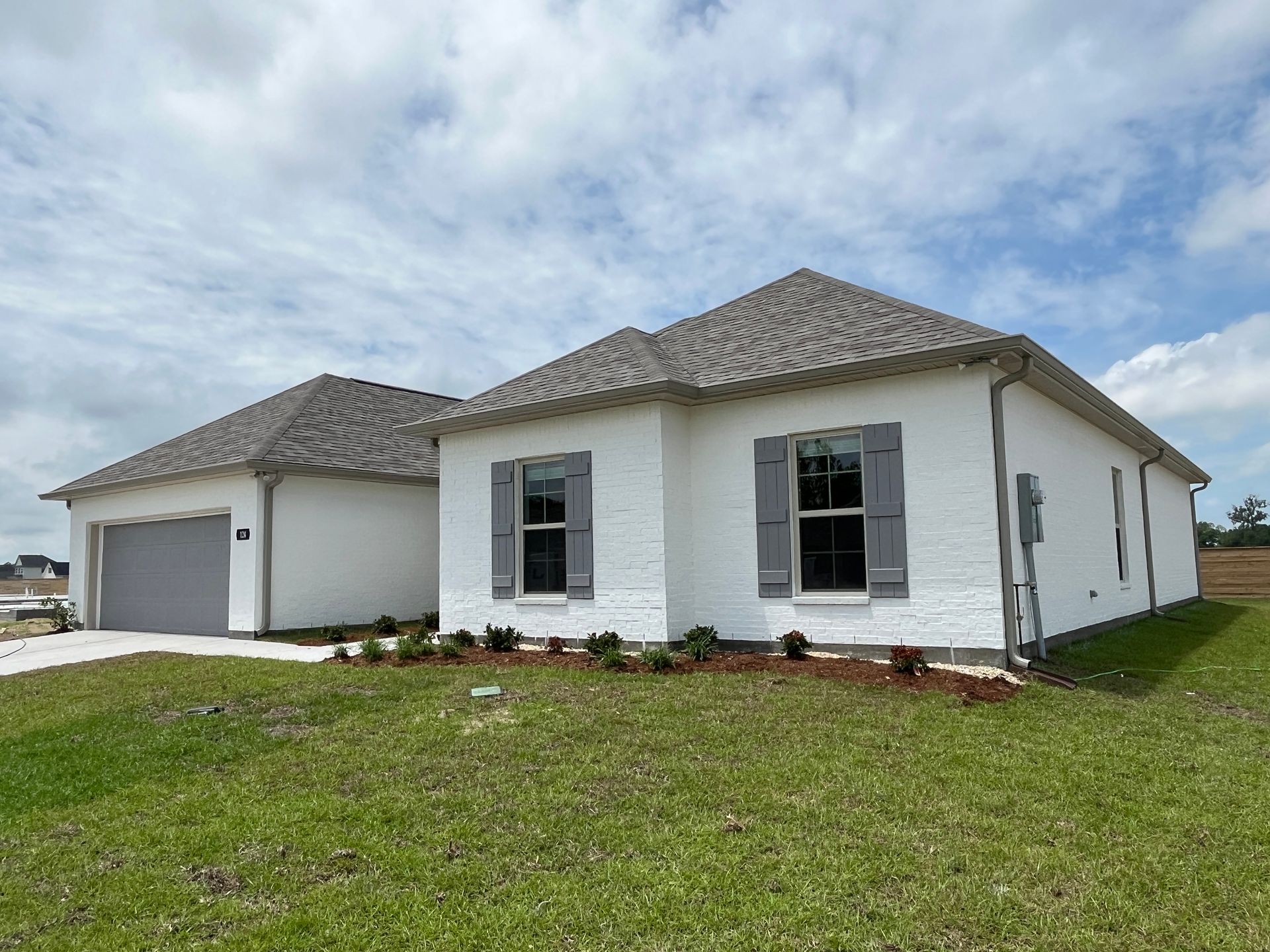 A single-story white brick house with a gray roof, matching gray shutters, and an attached two-car garage.