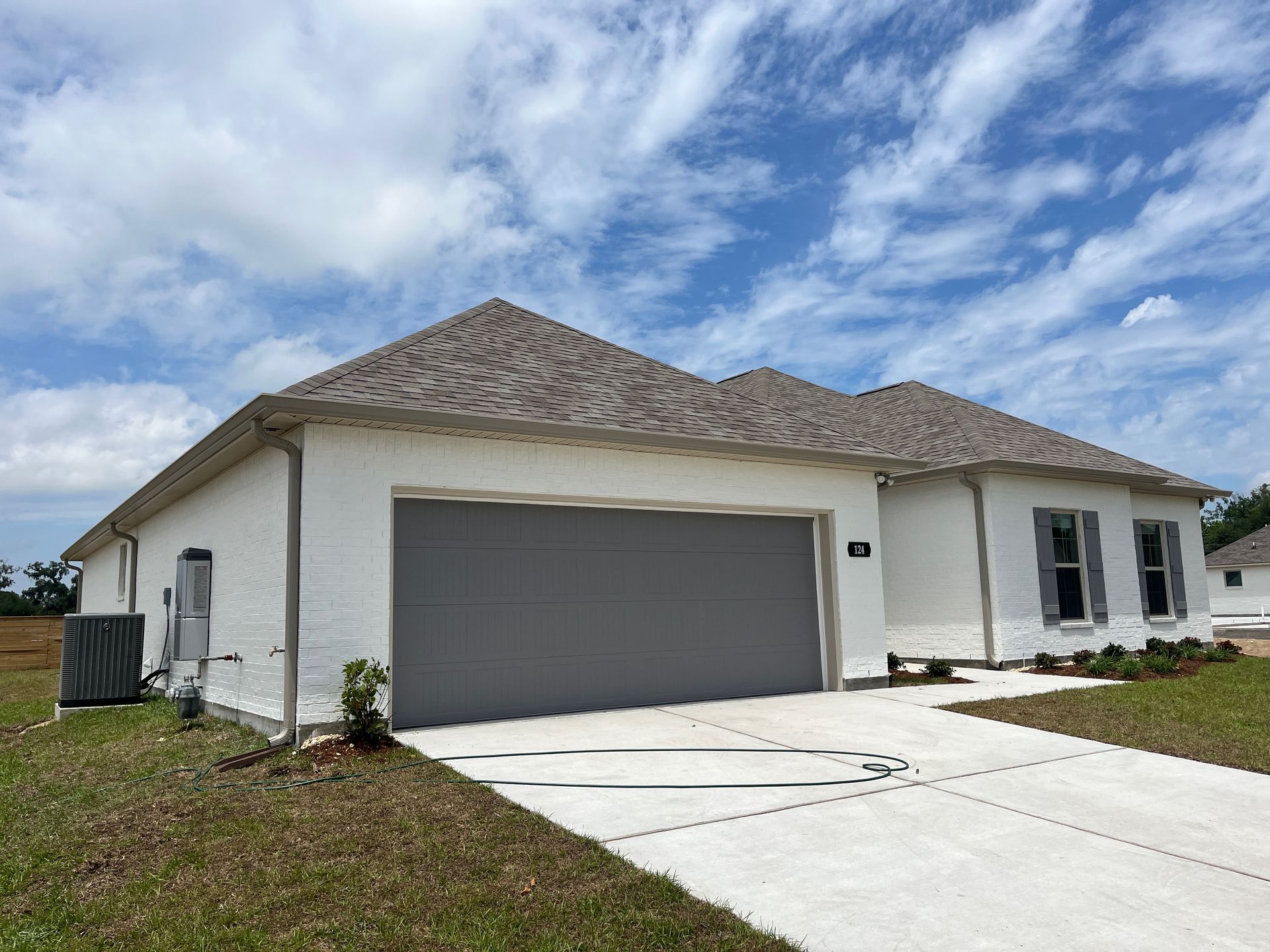 Single-story white brick house with a gray two-car garage, concrete driveway, and gray shingled roof under a blue sky.