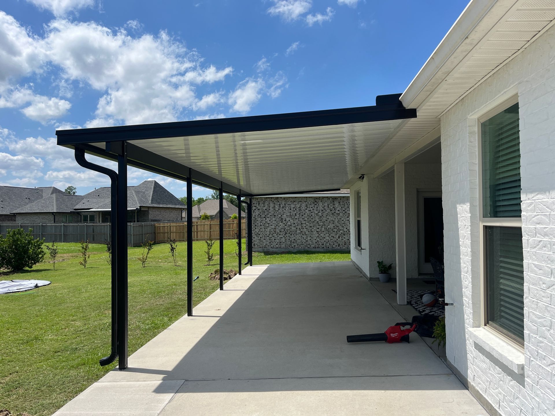A white brick house with a black covered patio roof supported by black posts, overlooking a grassy backyard.