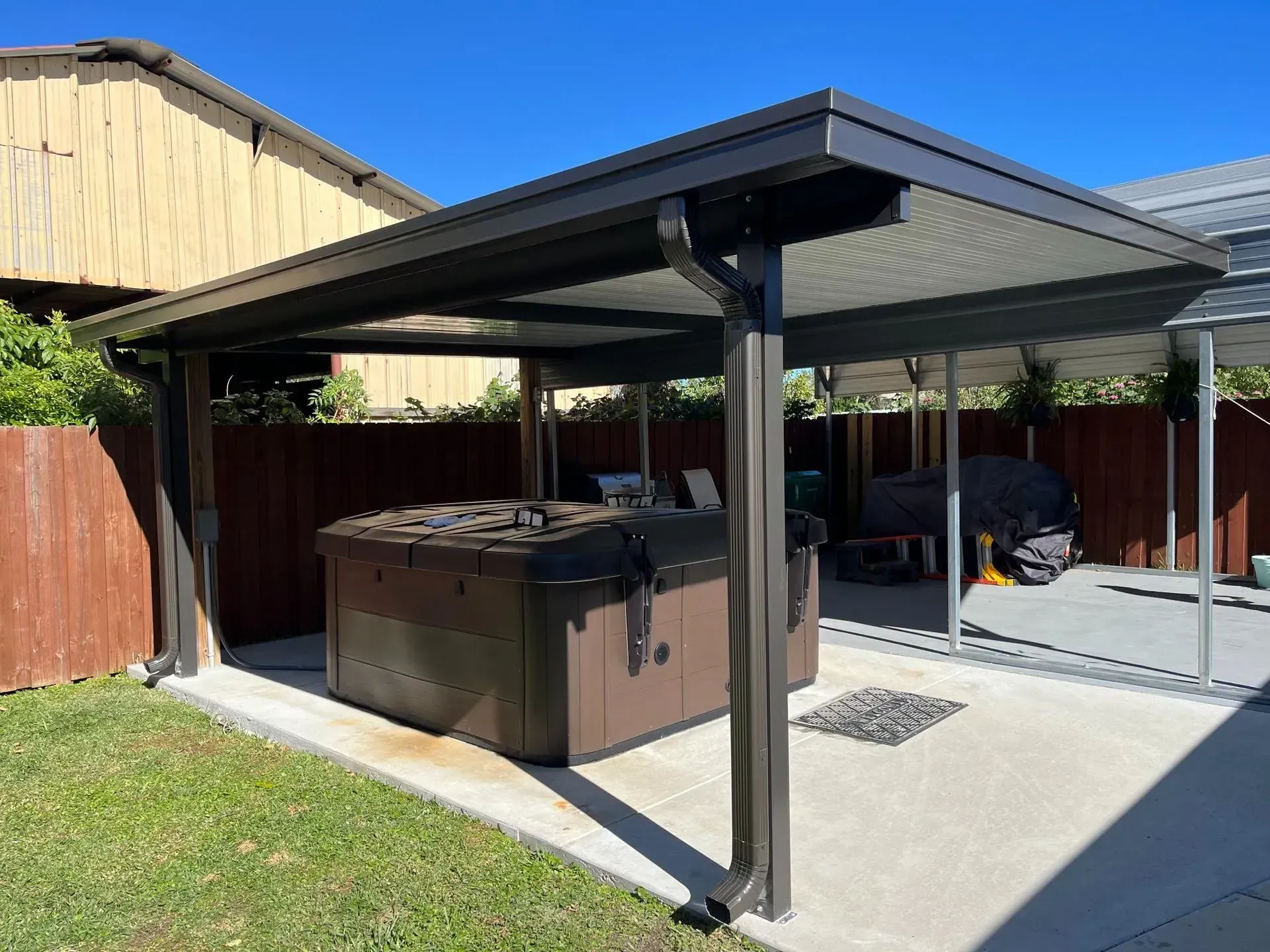 Backyard patio with a black-roofed pergola covering a hot tub and concrete seating area