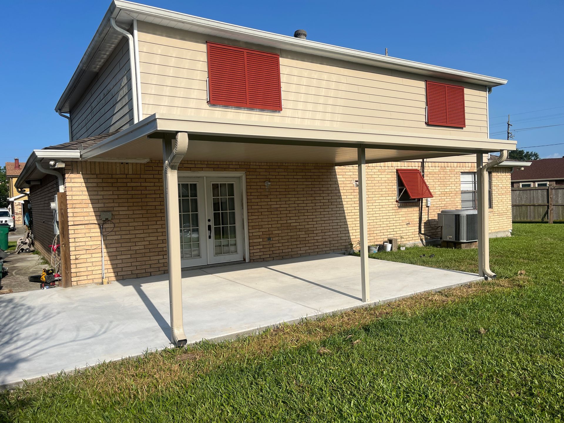 A two-story house with a tan brick lower level, light siding upper level, red shutters, and a covered back patio.