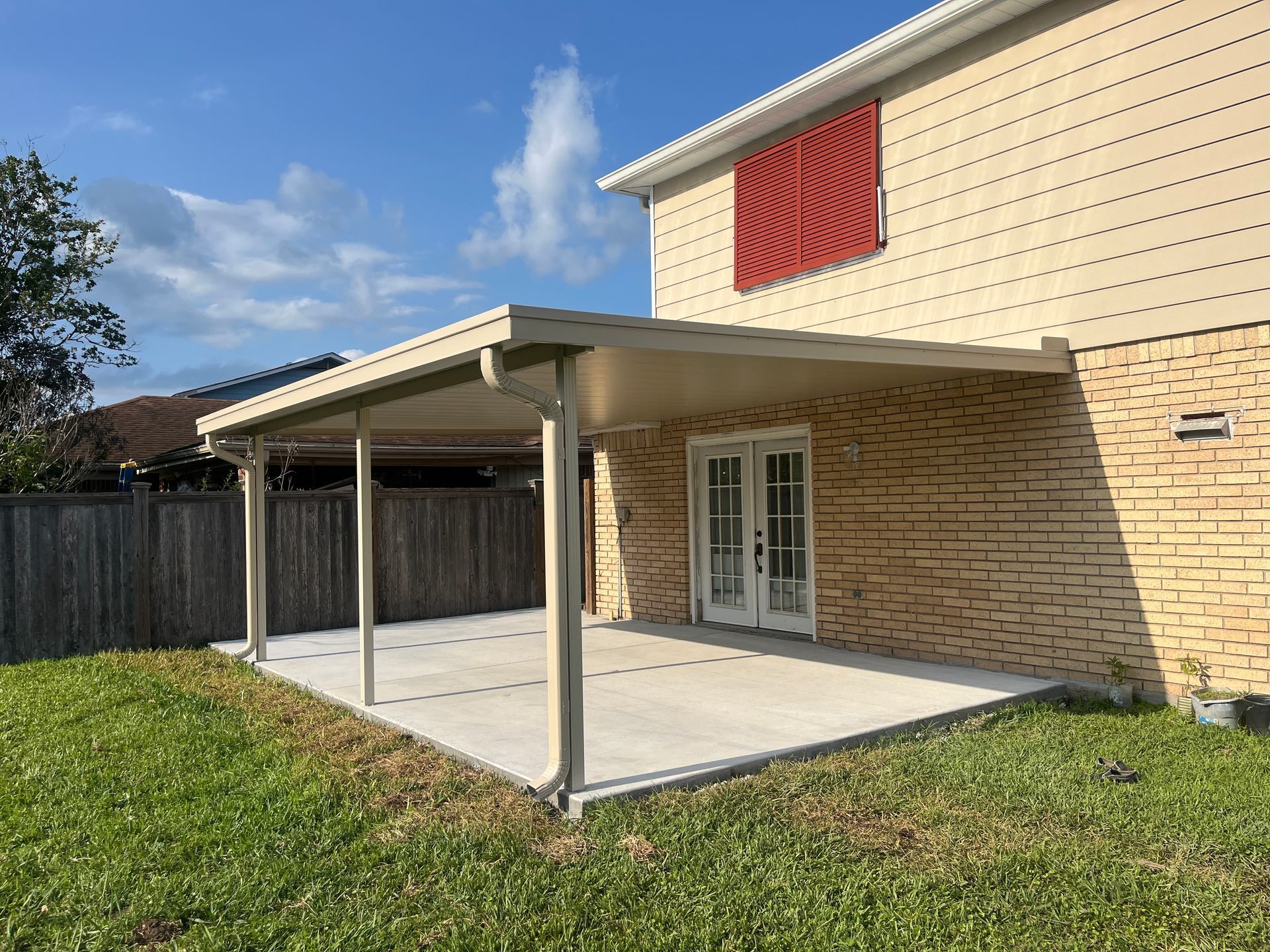 A tan house with a brick lower level, white French doors, and a covered patio area in the backyard.