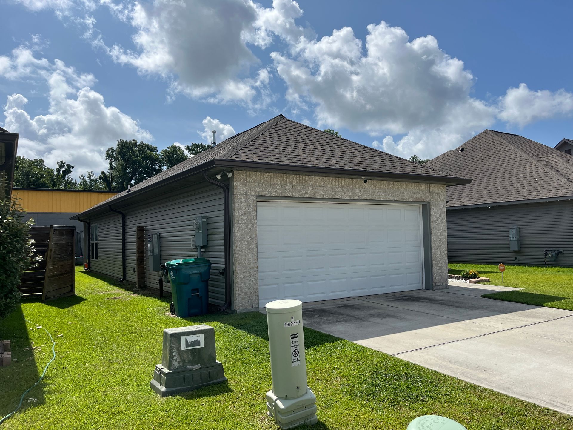 A residential detached garage with light stone and dark gray siding under a cloudy blue sky.