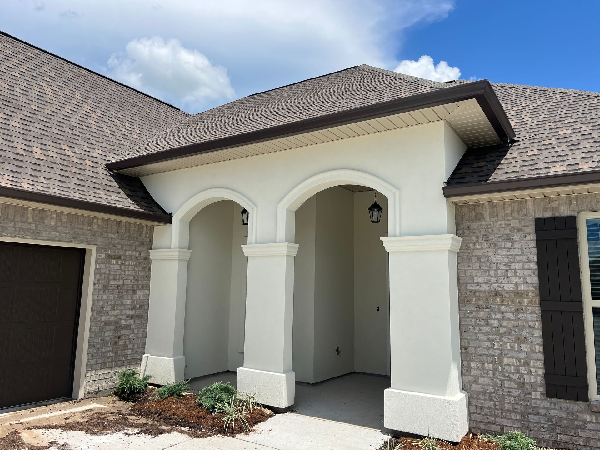 A front view of a house entrance with an arched, white stucco porch supported by three columns, and brick exterior walls.