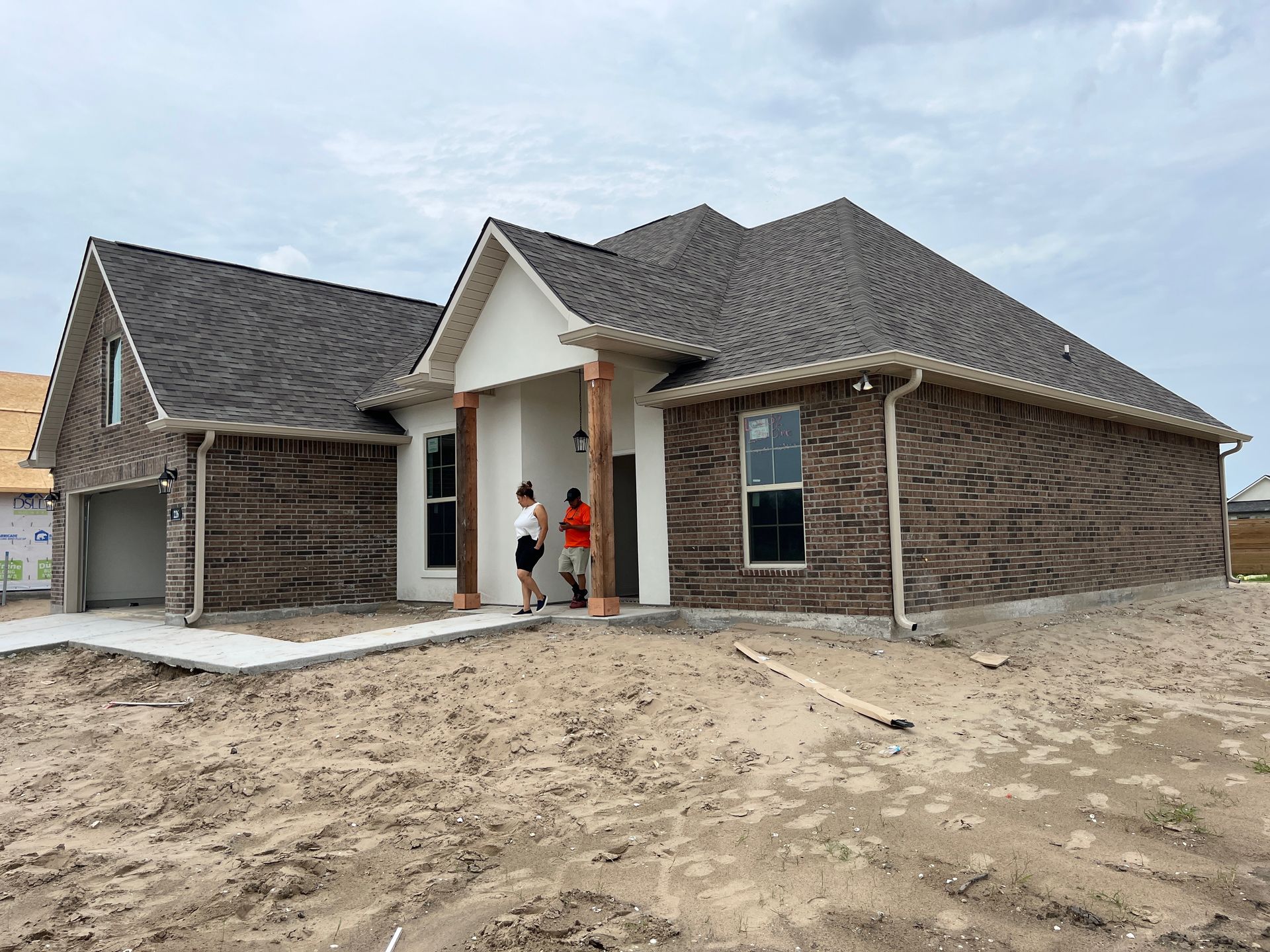 A newly constructed single-story brick home with a gray roof and two people standing at the entrance.