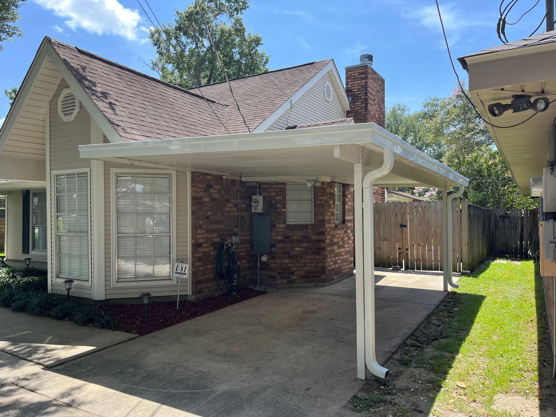 A beige, single-story house with a brick exterior and a white attached carport on a sunny day.