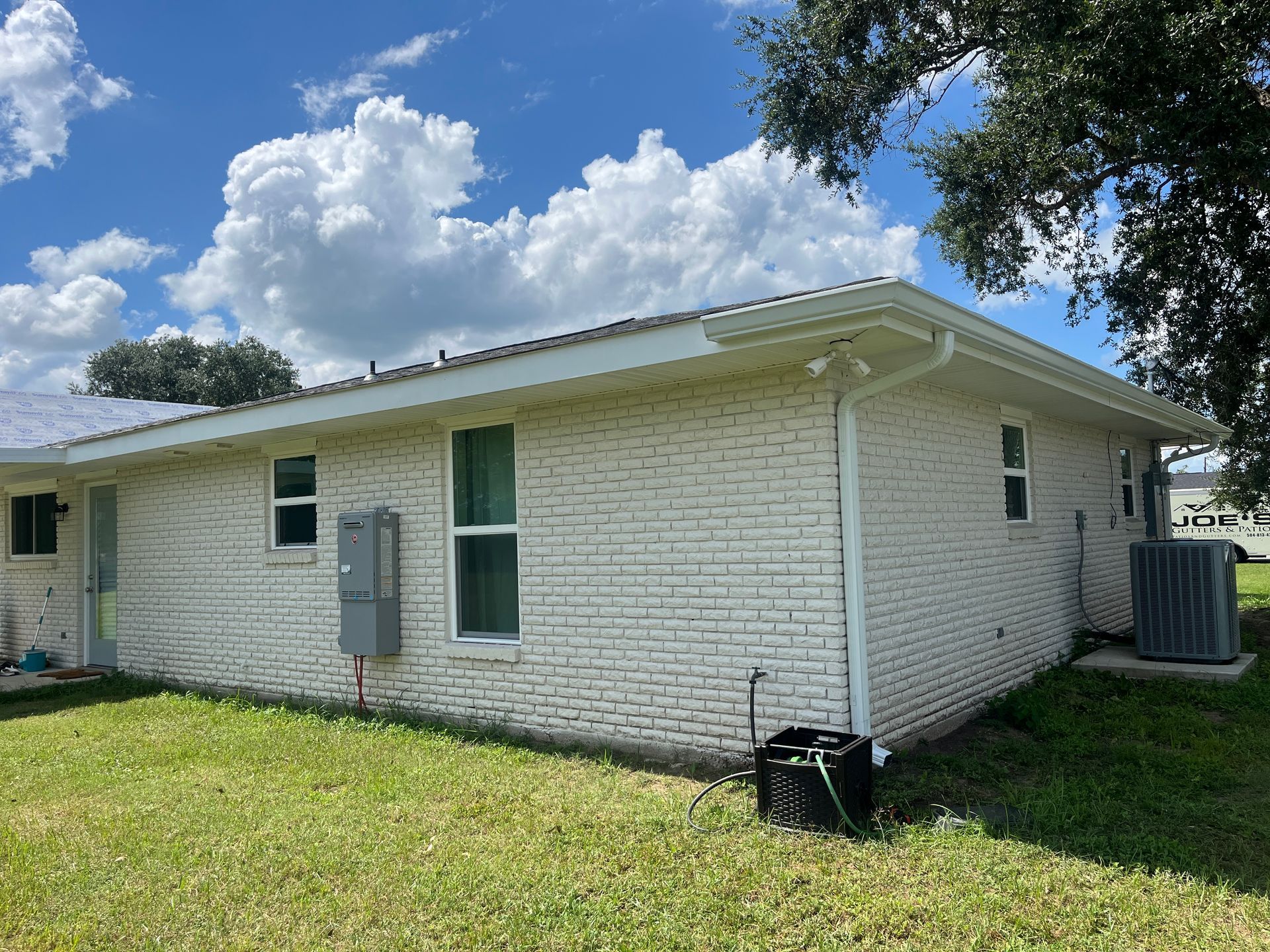A side view of a white brick house with a dark roof under a blue sky with fluffy white clouds.