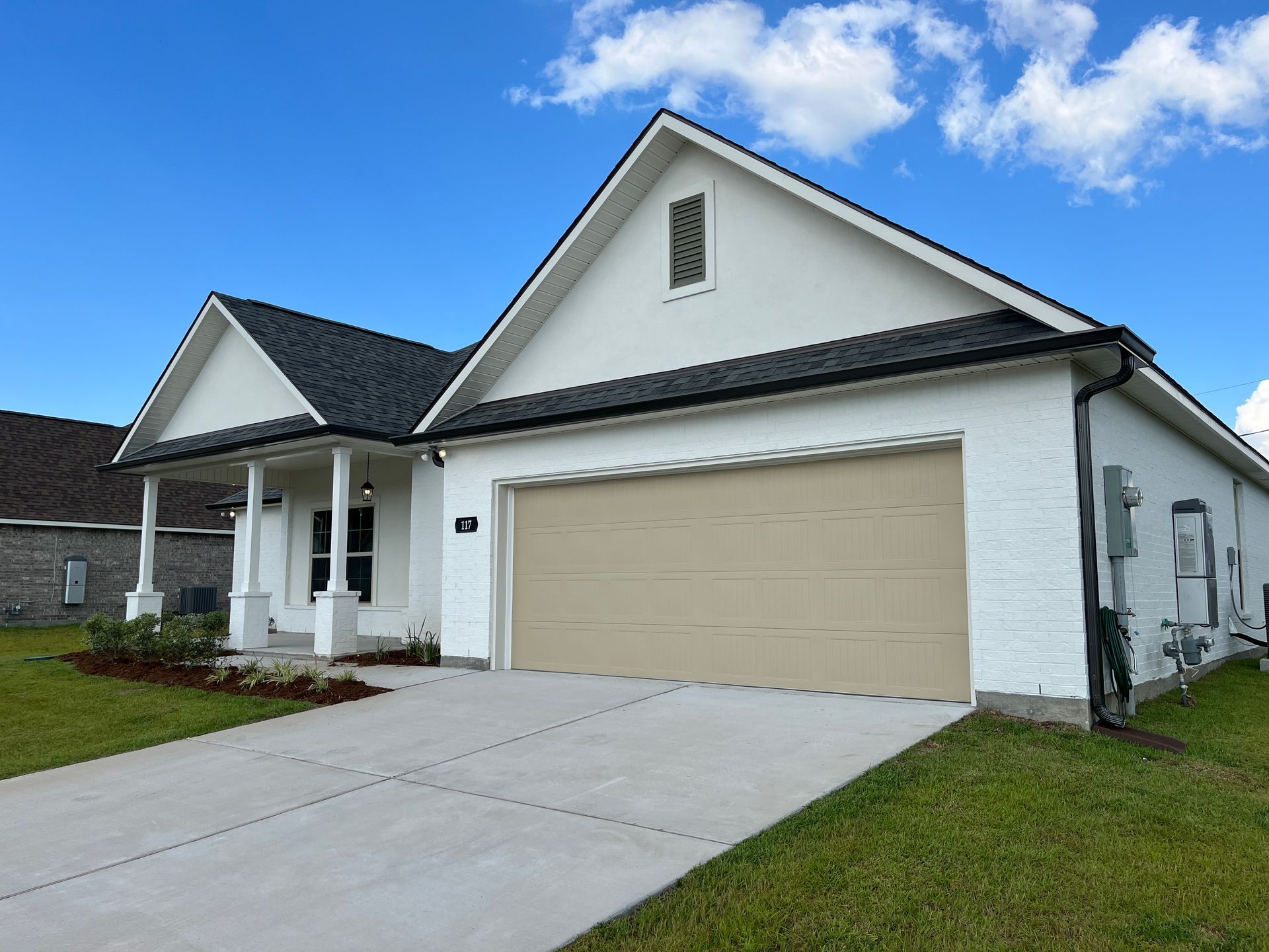 A single-story white brick house with a dark roof and a tan garage door under a bright blue sky.