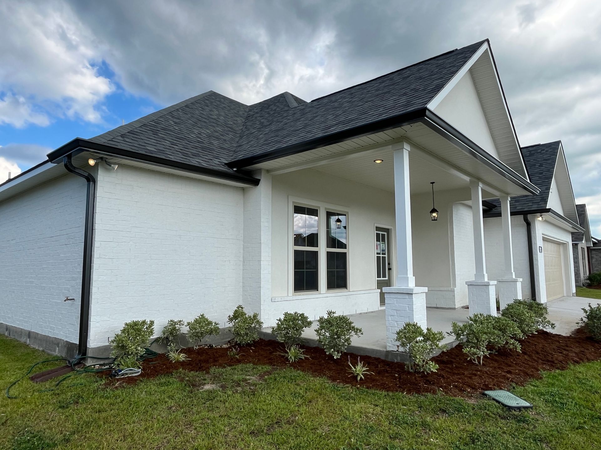 A newly constructed, single-story white brick house with a dark roof and a covered front porch featuring white columns.
